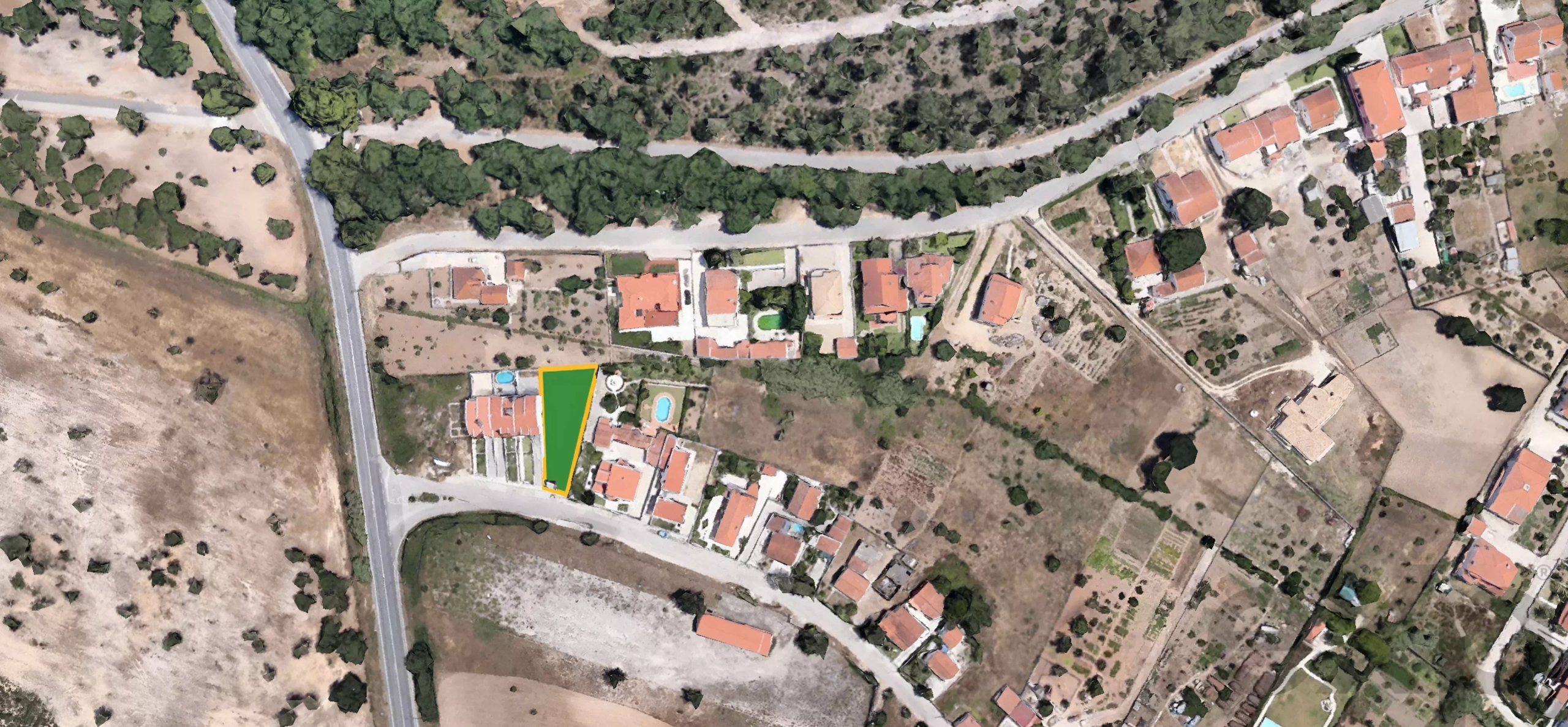 Aerial view of a residential area; a large triangular plot shaded green with a yellow border sits among houses and roads.