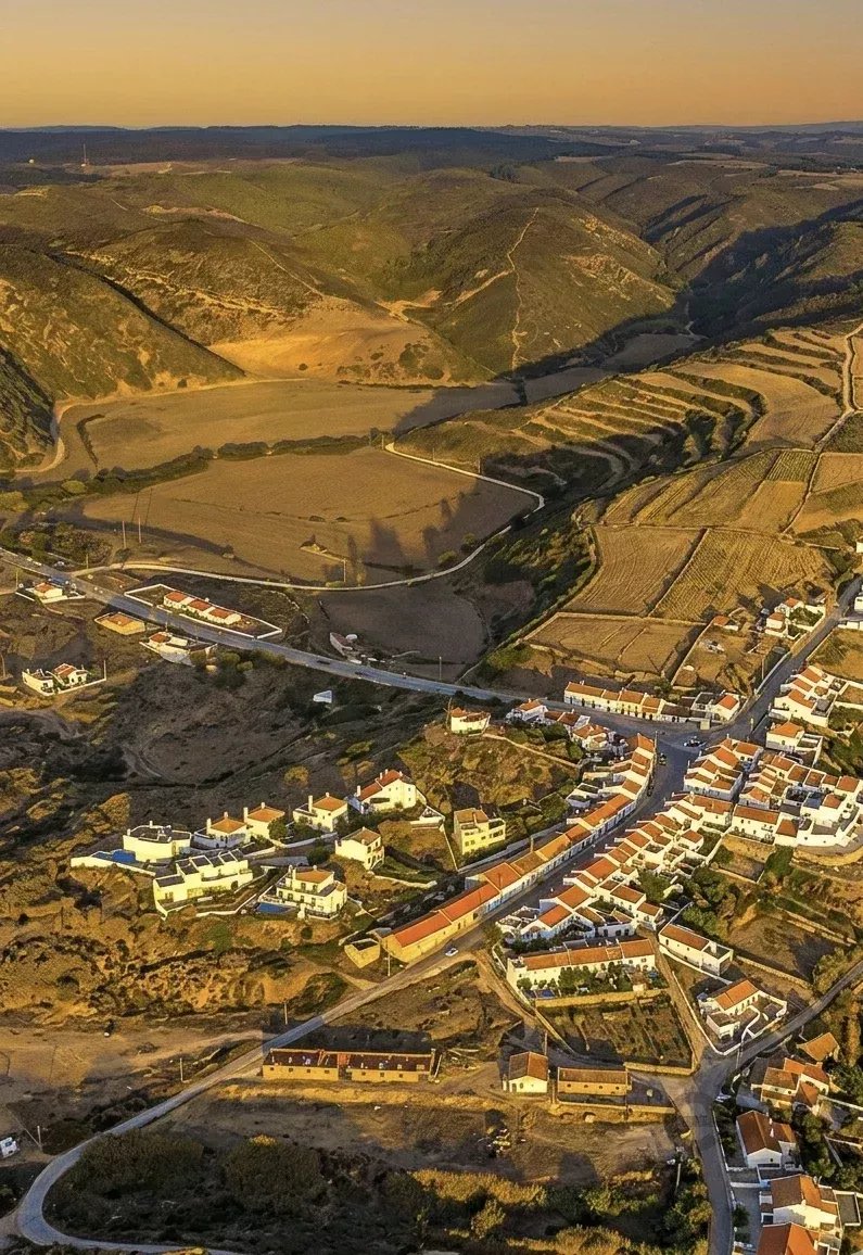 Aerial view of hillside village at sunset, with terraced fields and orange-roofed houses.