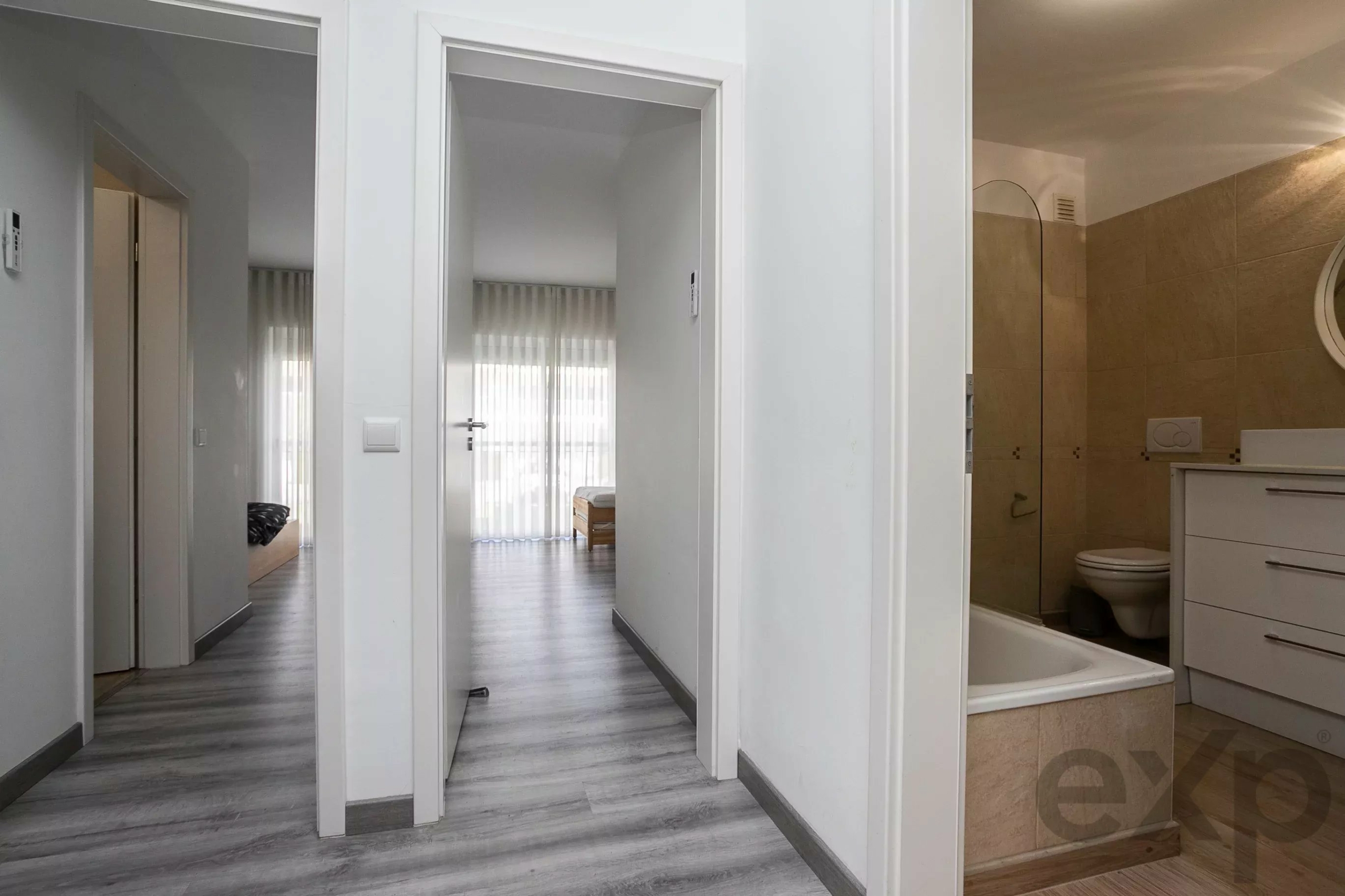 Bright hallway with white doors; glimpse of a sunlit bedroom through an open doorway and a tiled bathroom on the right.] , but fix quotes.