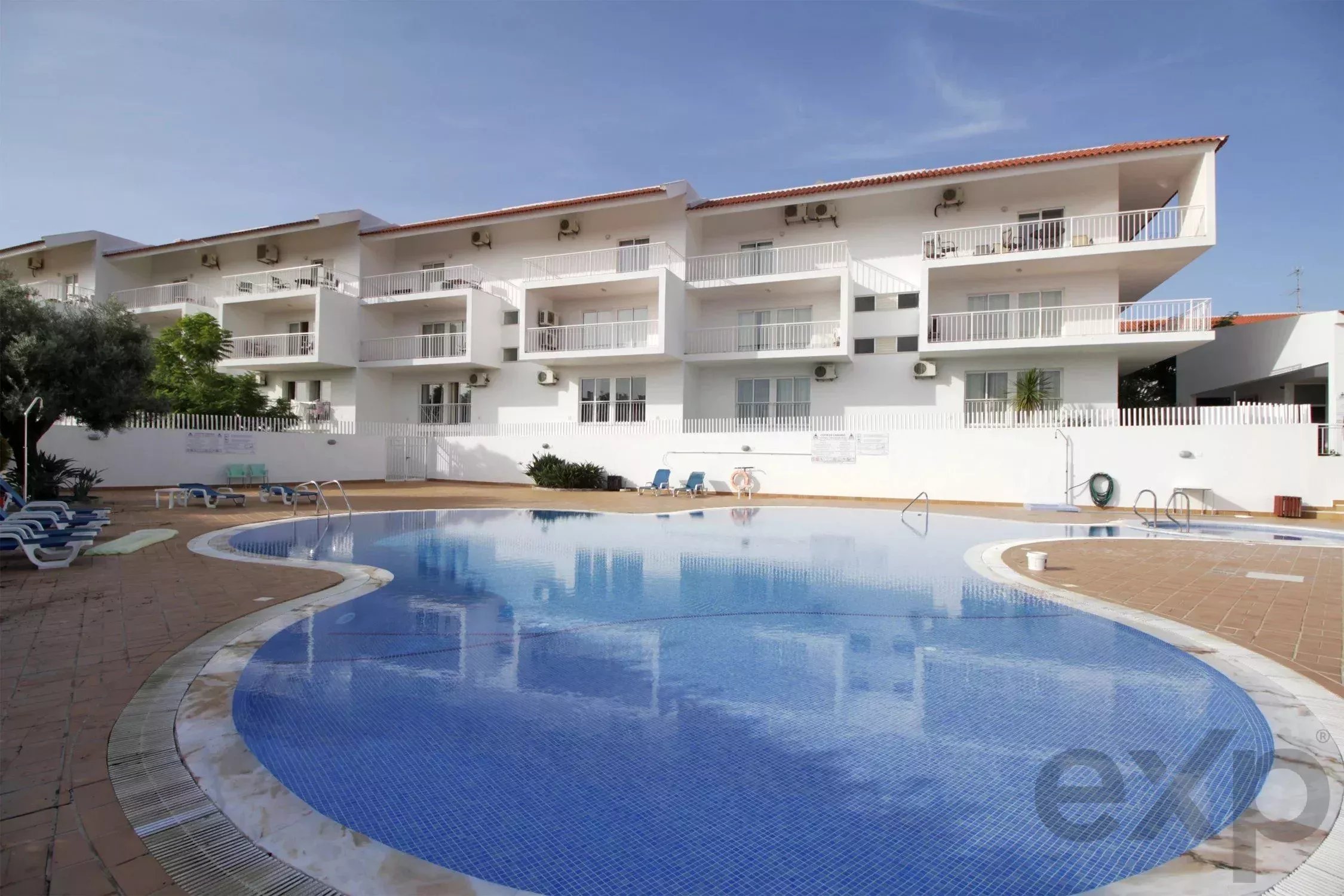 White multi-story apartment building with balconies surrounding a blue pool area.