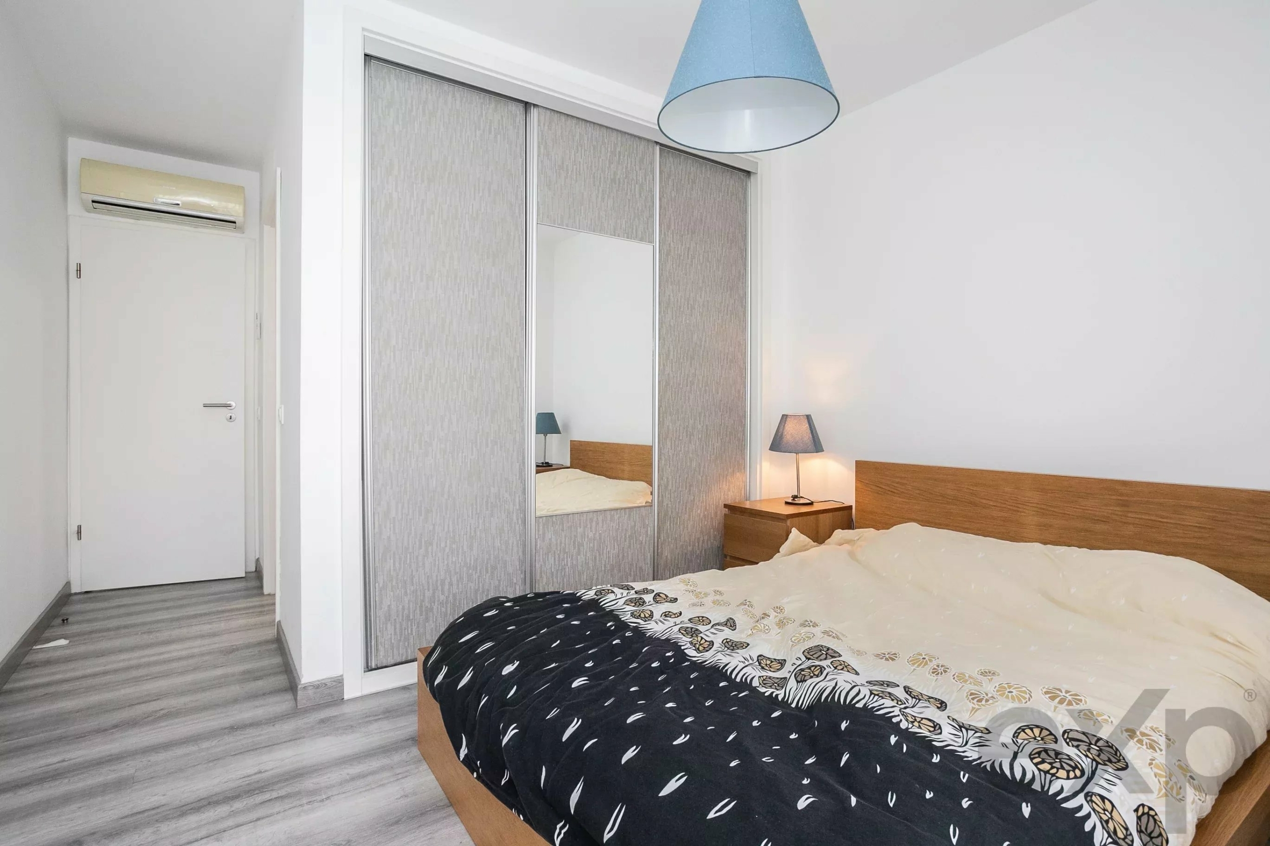 Bedroom with wooden bed, large sliding wardrobe with mirrored panels, and a blue pendant lamp hanging from the ceiling.