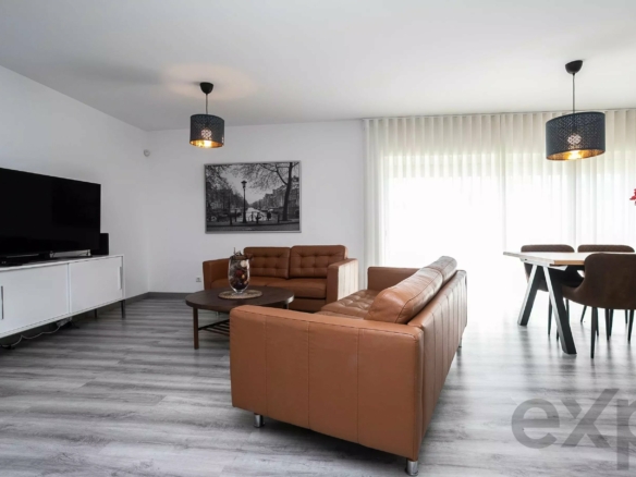 Bright living room with brown leather sofa set, a TV on a white cabinet, and large windows with vertical blinds