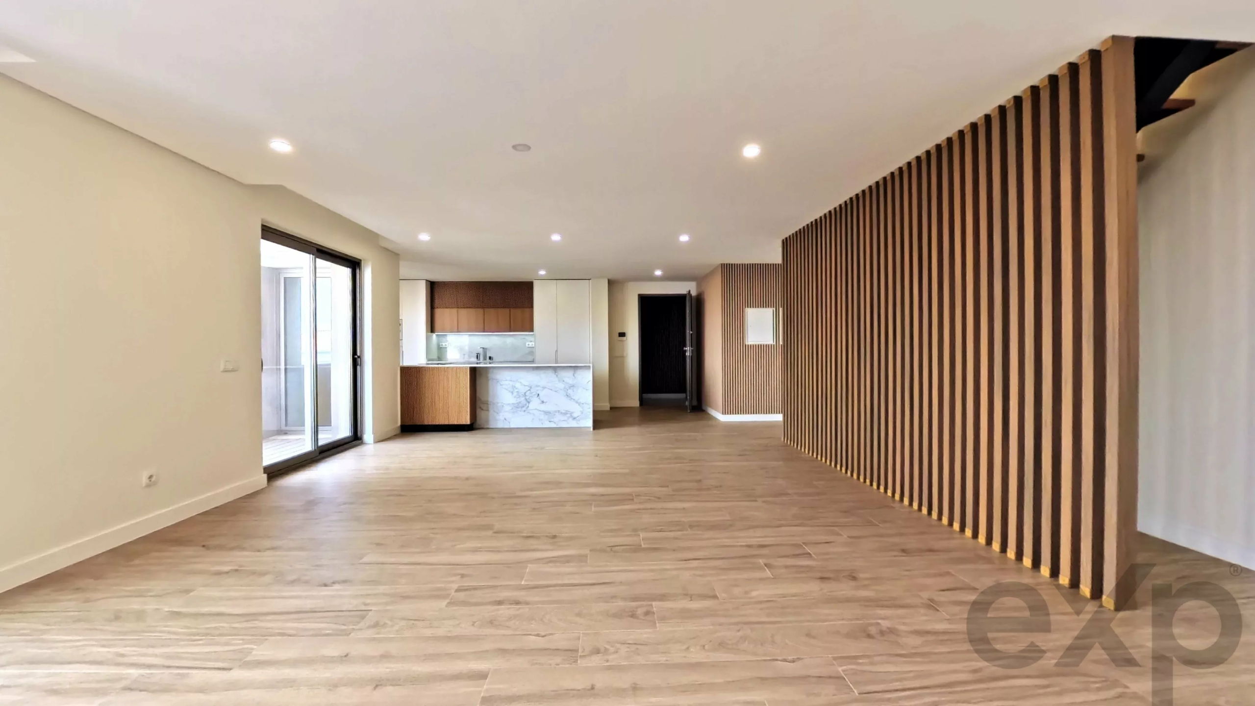 Open-concept living area with a kitchen island, sliding doors to the outside, and a tall wooden slat divider along one wall.