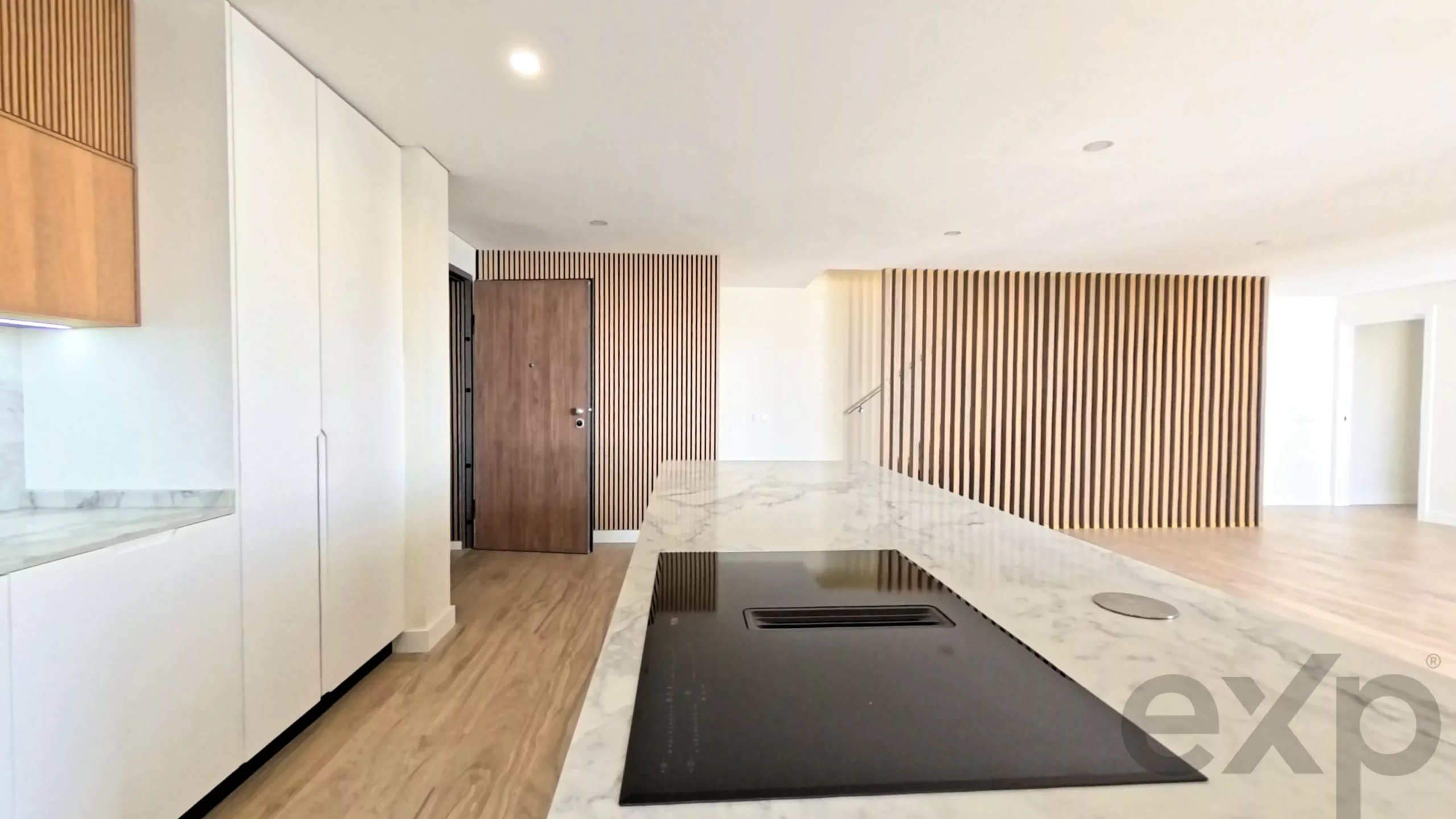 Bright modern kitchen with a marble island, black induction cooktop, white cabinets, and a wood slat wall.