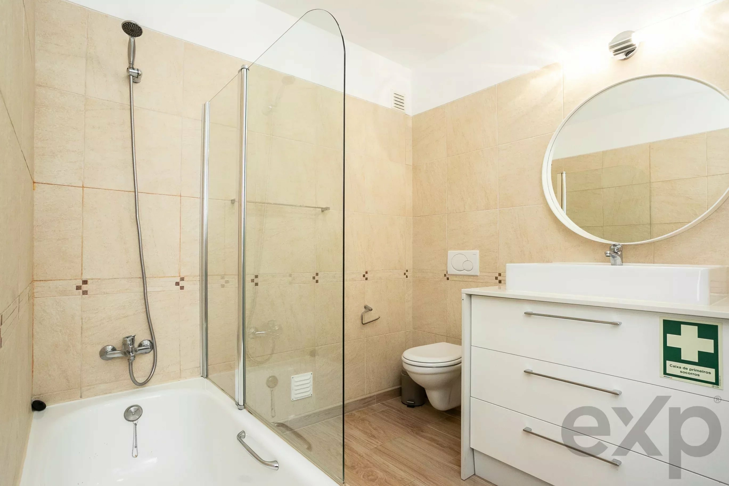 Modern bathroom with a glass shower enclosure, bathtub, and a white vanity with a circular mirror on the wall.