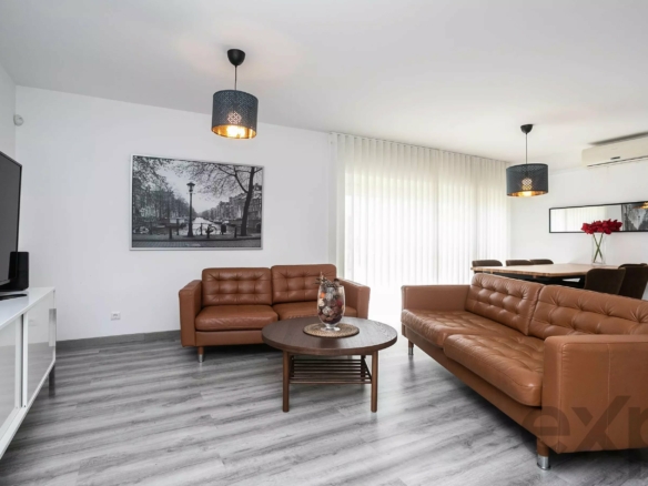 Modern living room with brown leather sofas, a round coffee table, wall art, and large windows with vertical blinds.