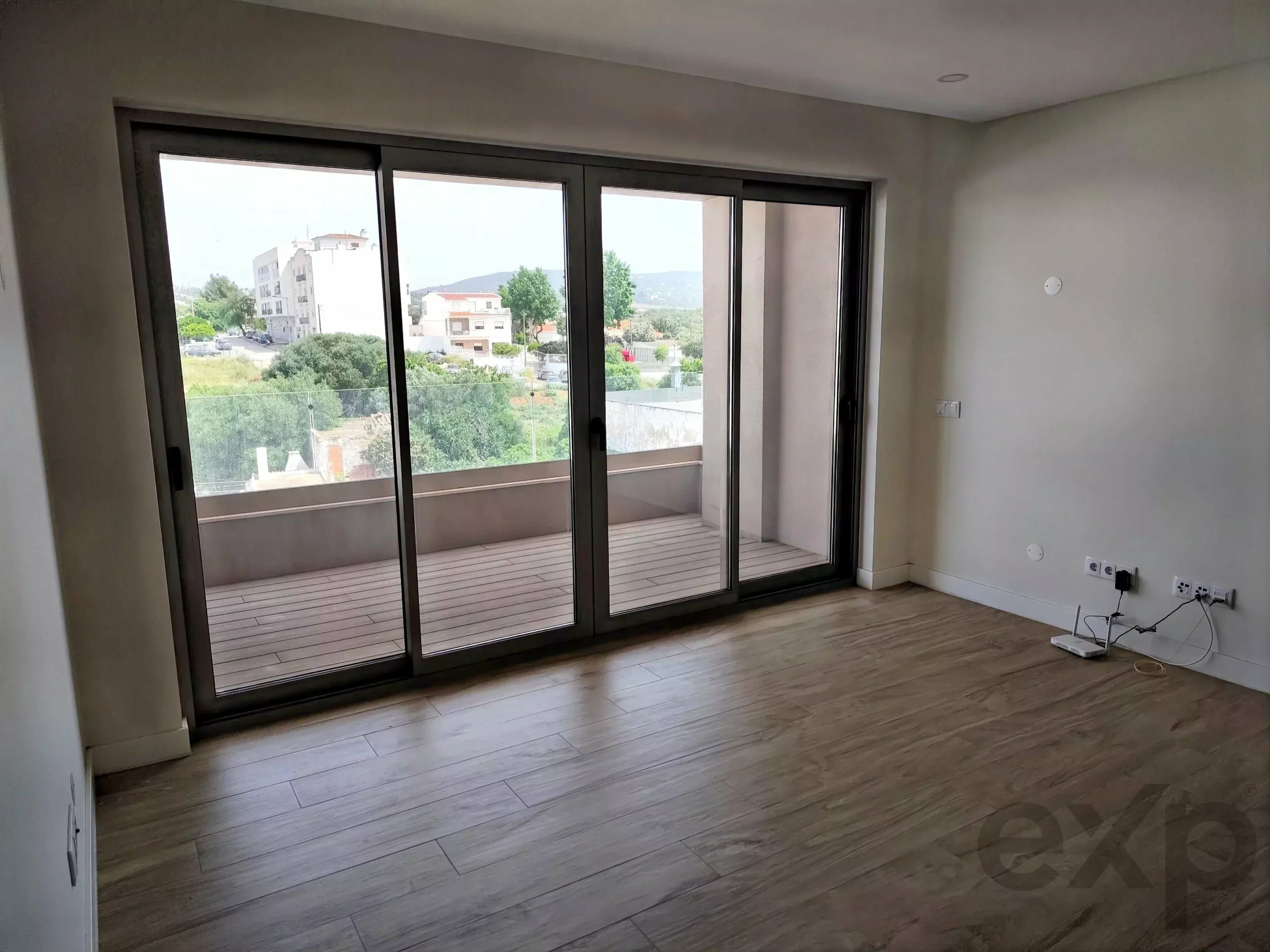 Living room with large sliding glass doors opening to a balcony; view of buildings and hills outside.