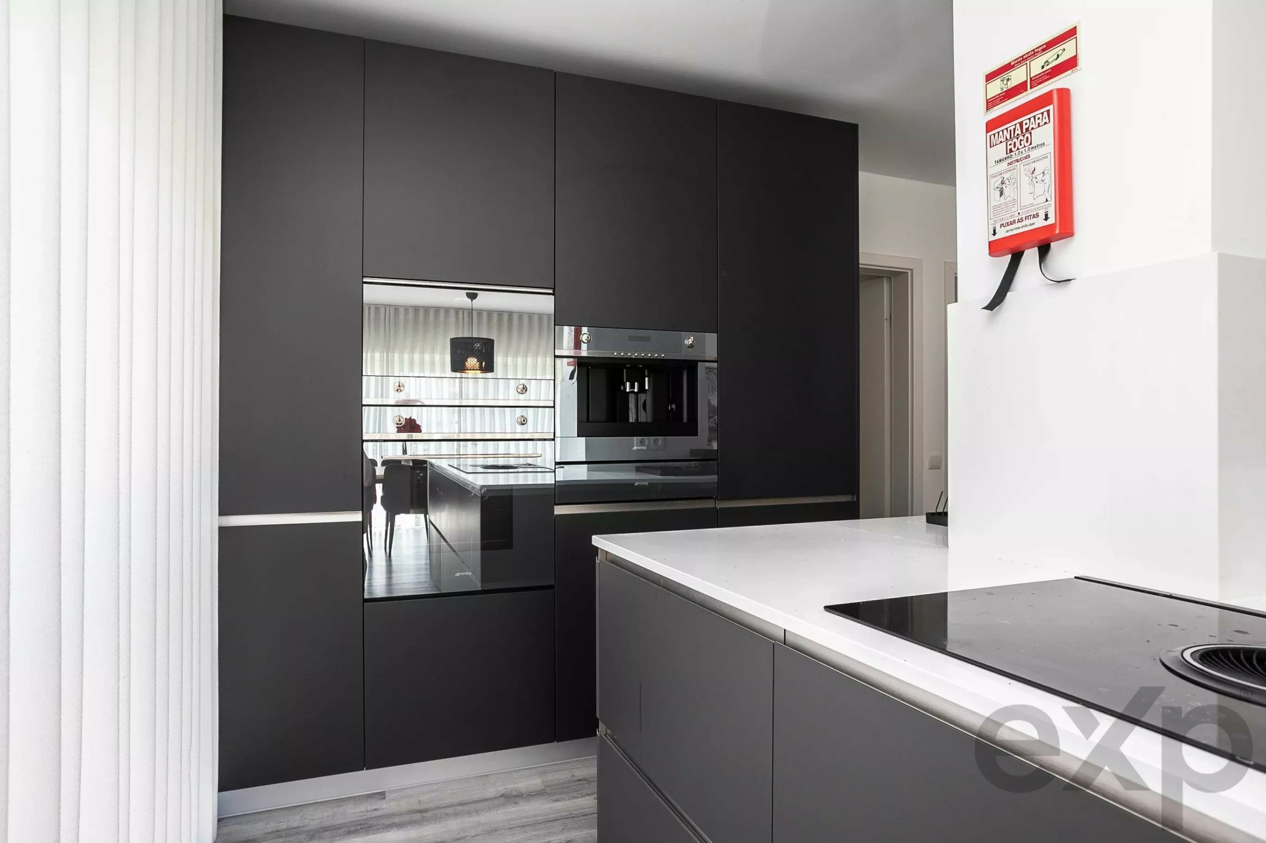 Modern kitchen with tall dark cabinets, built-in oven, and a white countertop island; a red fire extinguisher on the wall.