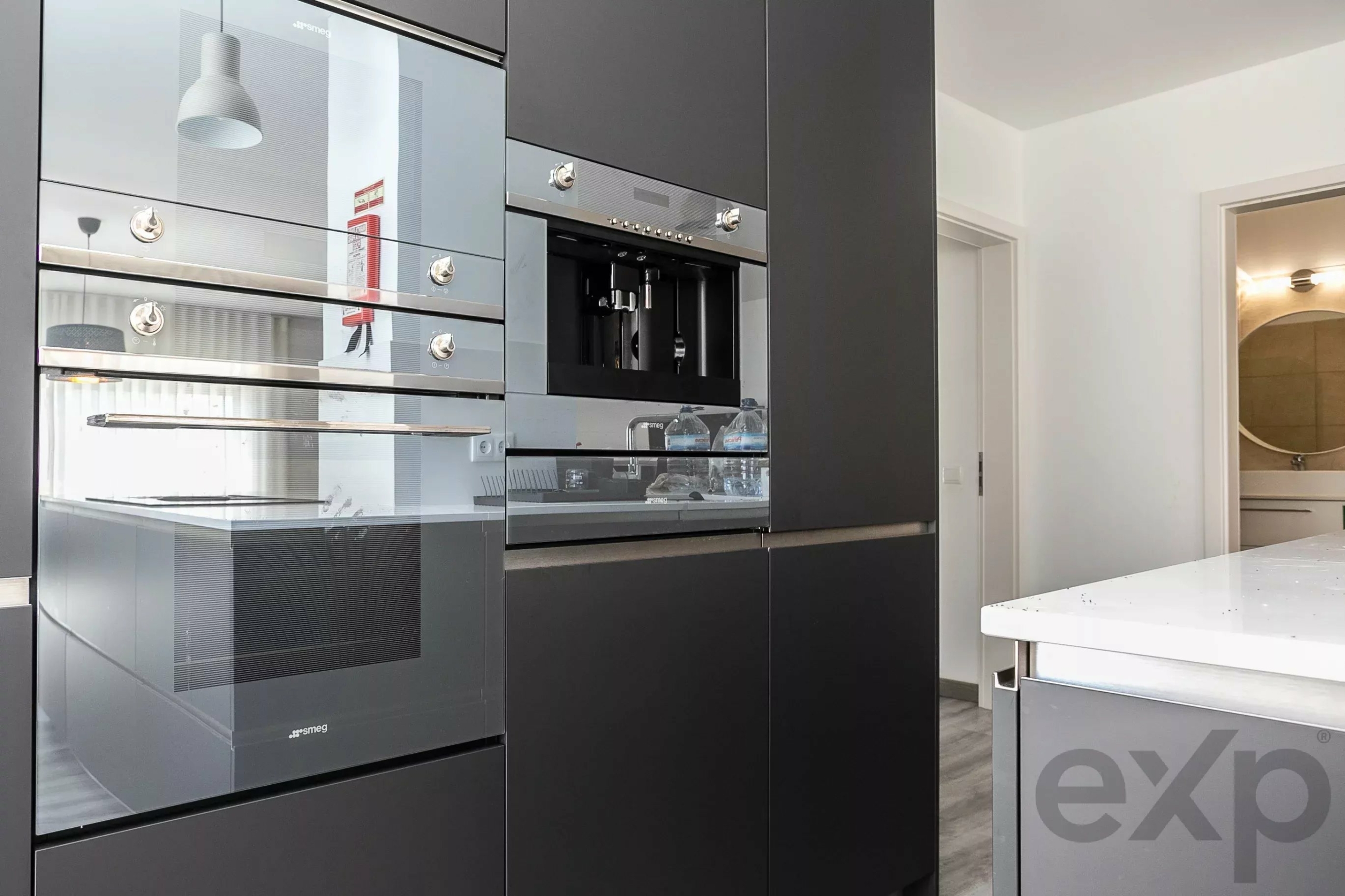 Modern kitchen with built‑in stainless steel ovens set in dark grey cabinets, glass doors reflecting light.