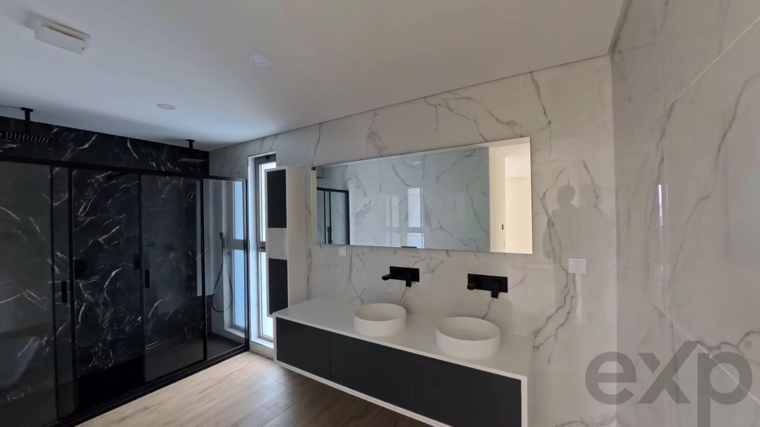 Modern bathroom with marble walls, a double-sink vanity, and a black-framed glass shower.