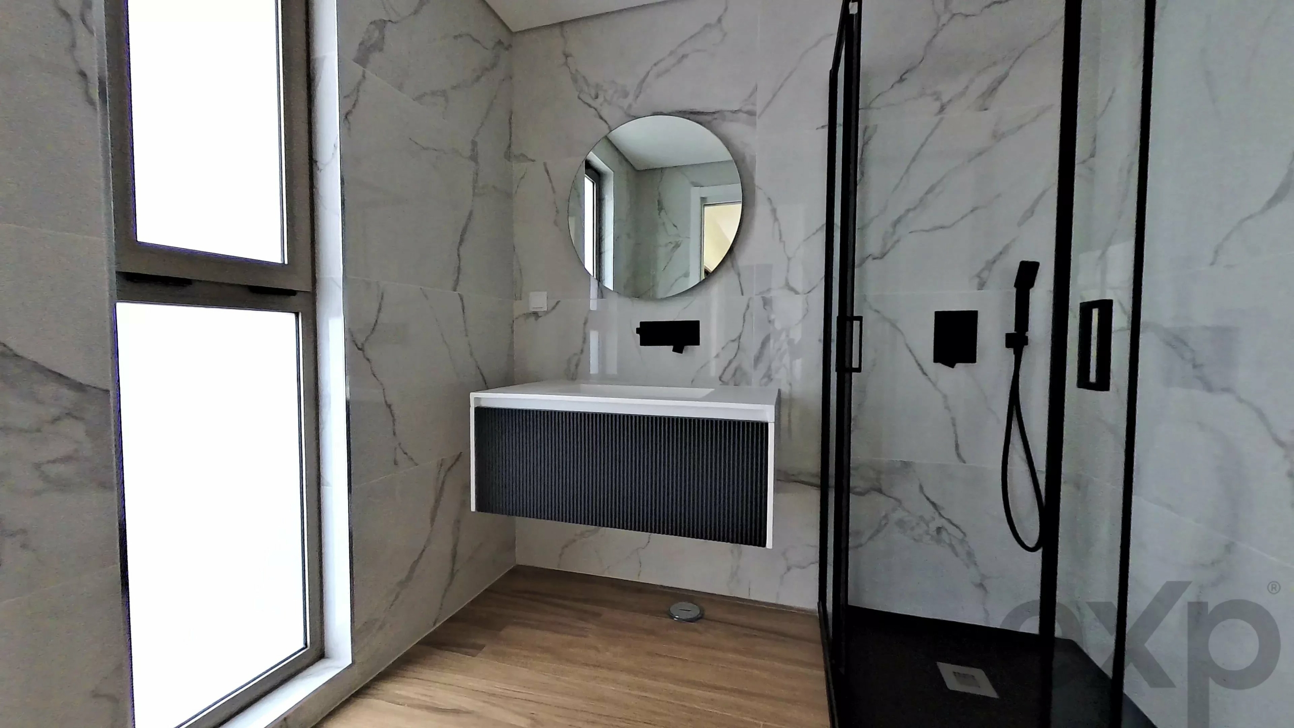 Modern bathroom with marble walls, a round mirror, floating white sink, and a glass shower with black fixtures for a minimalist look.