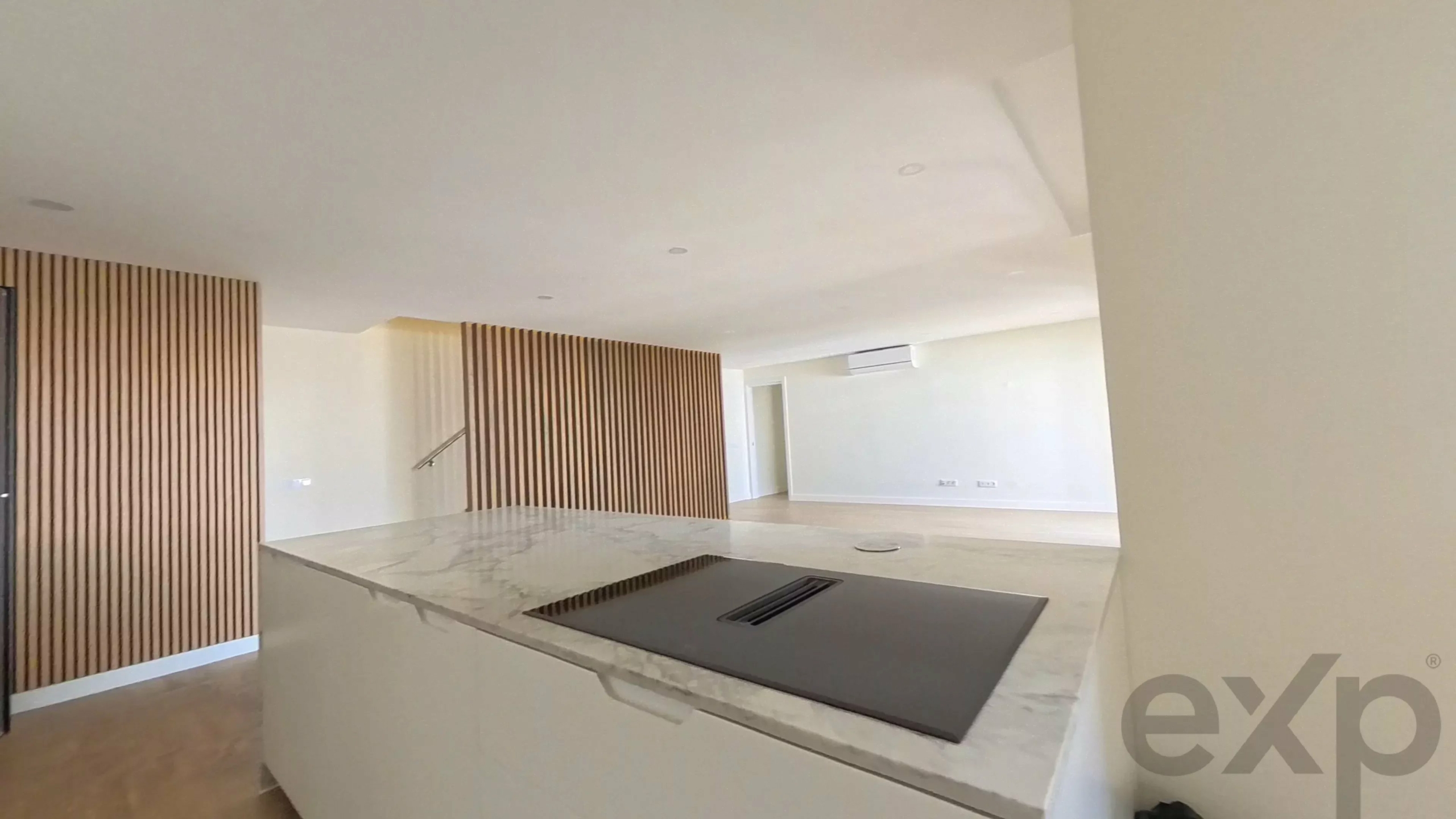 Modern kitchen with a marble island, built-in cooktop, and vertical wood slat divider.