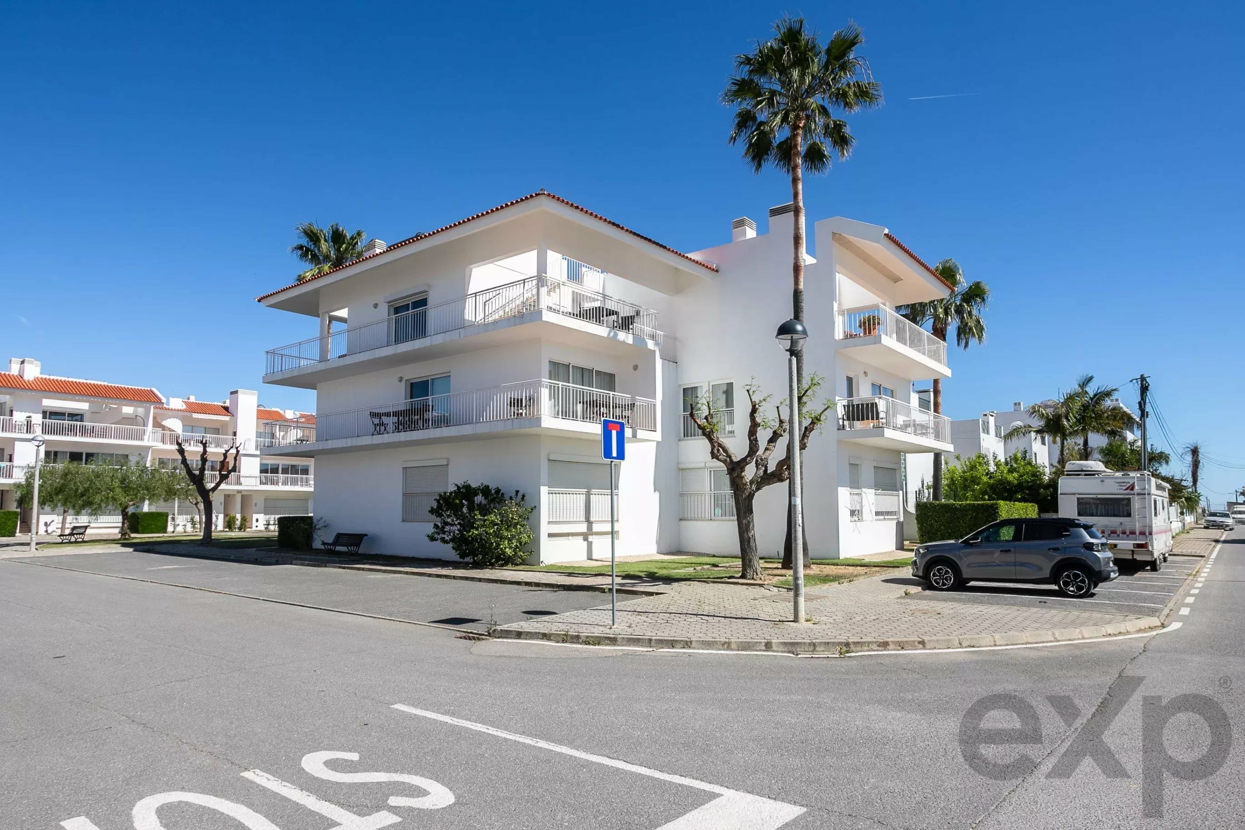 White multi-story apartment building with balconies and tall palm trees under a clear blue sky.
