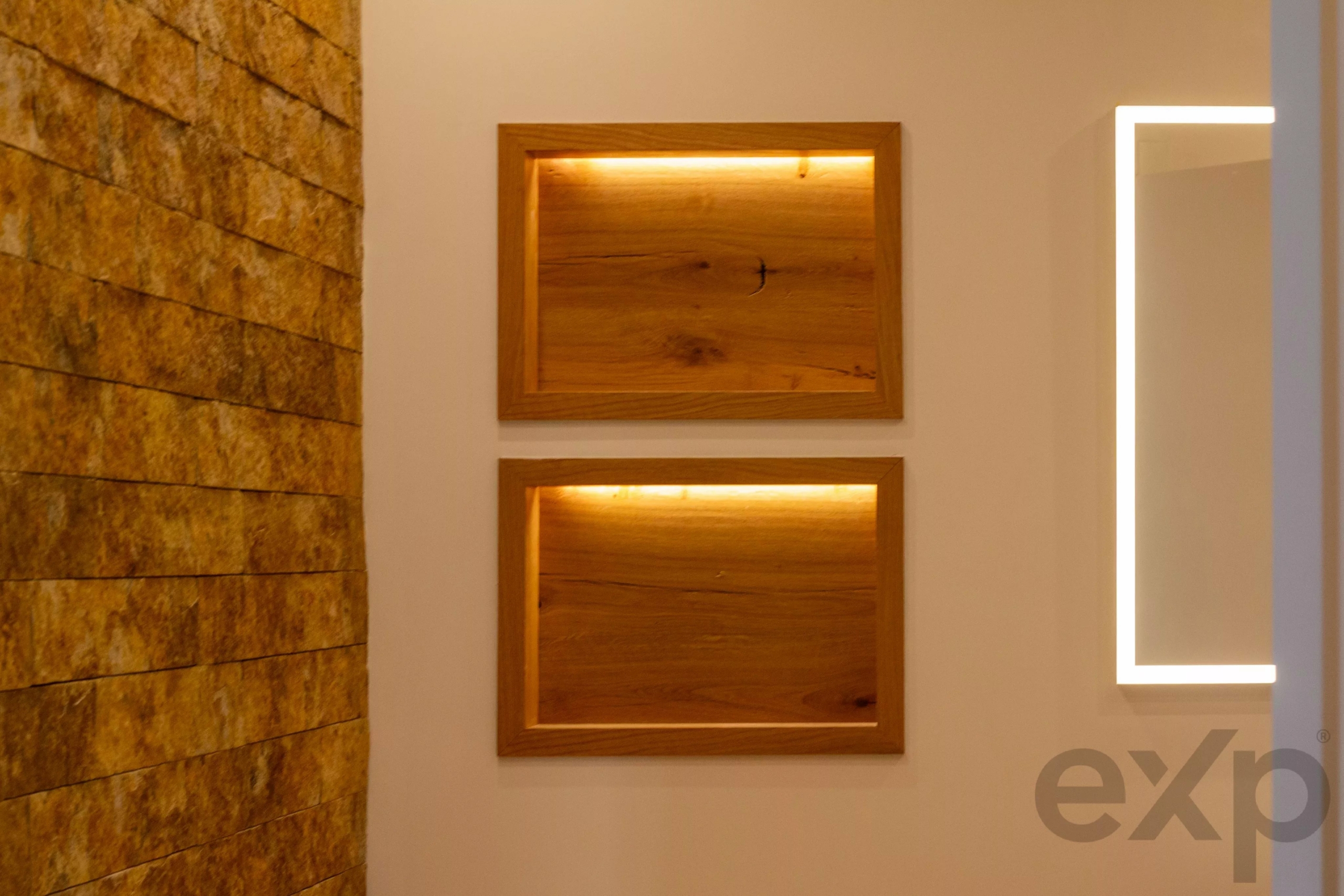 Beige wall with two warm-lit wooden display boxes and a stone panel on the left.