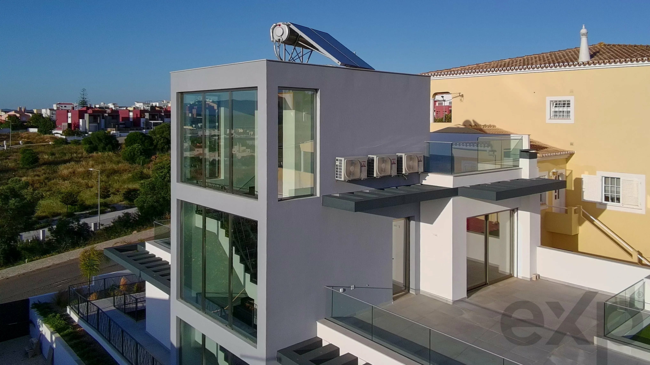 Modern grey, glass-front building with a rooftop solar water heater unit against a blue sky, glass balcony nearby.