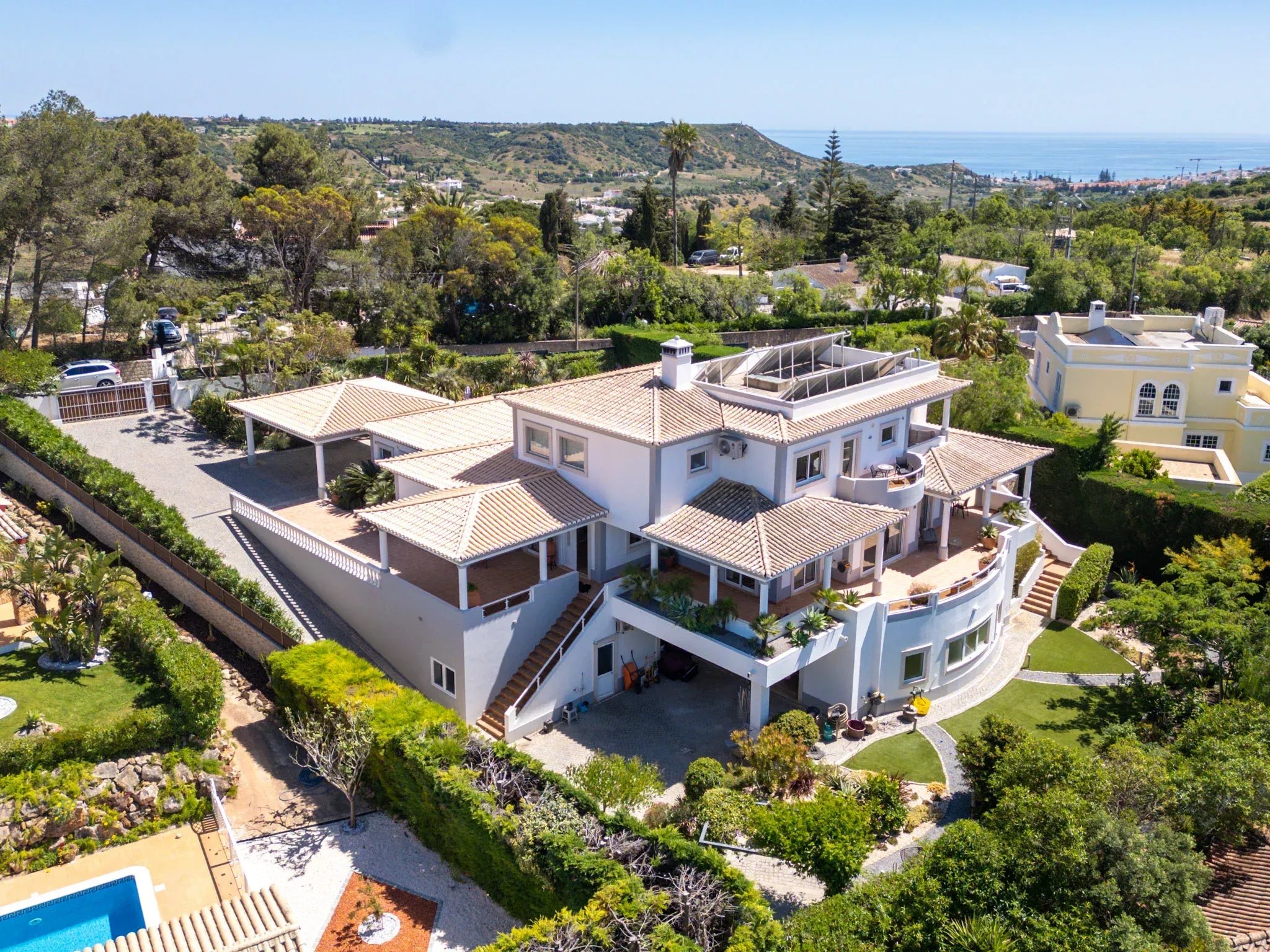 Aerial view of white Mediterranean-style houses with terracotta roofs on a hillside overlook the blue sea and distant coastline.
