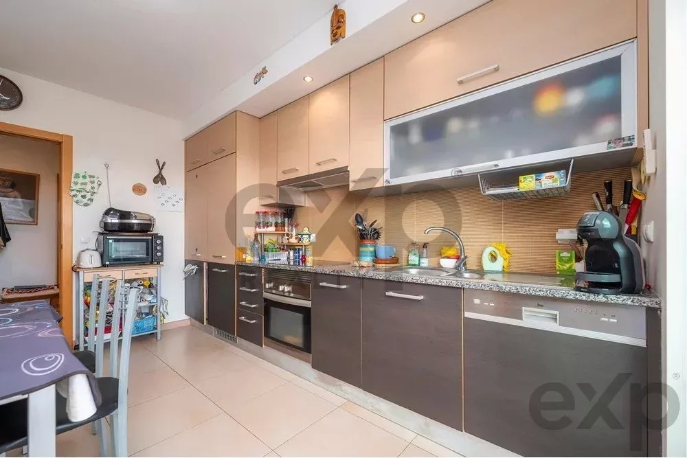 Compact kitchen with light wood upper cabinets and dark lower cabinets, stainless steel appliances, and a tiled backsplash.
