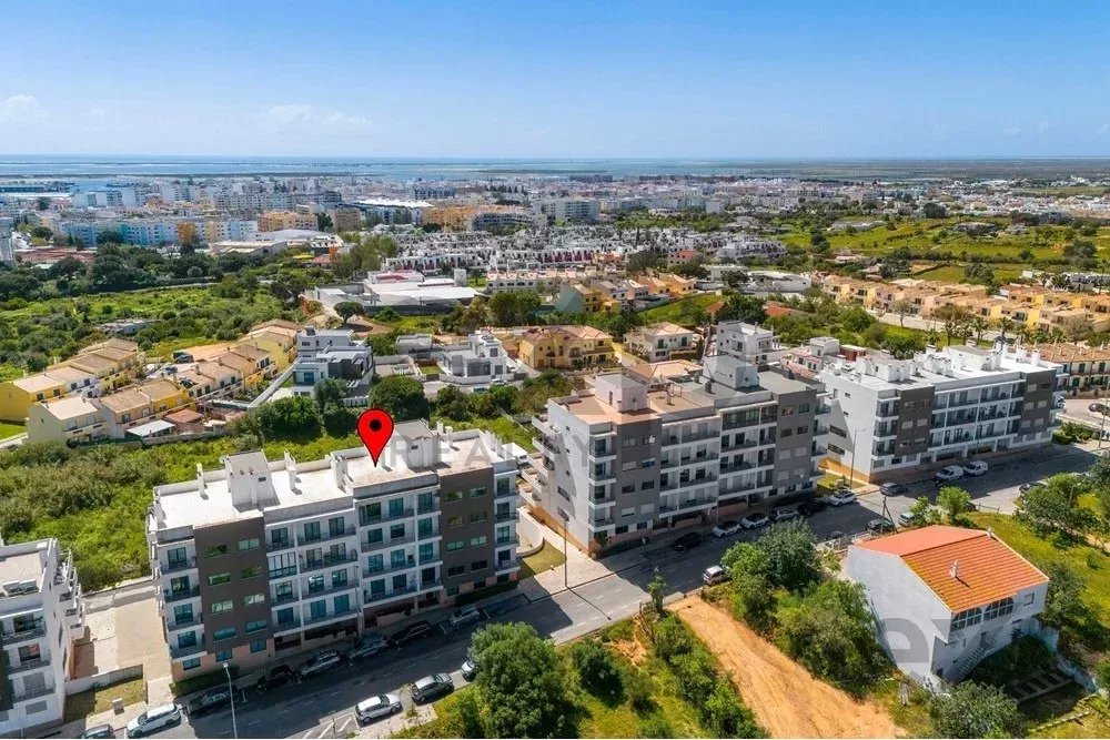Aerial view of a coastal residential area with modern apartment buildings; a red location pin sits on a rooftop in the foreground.
