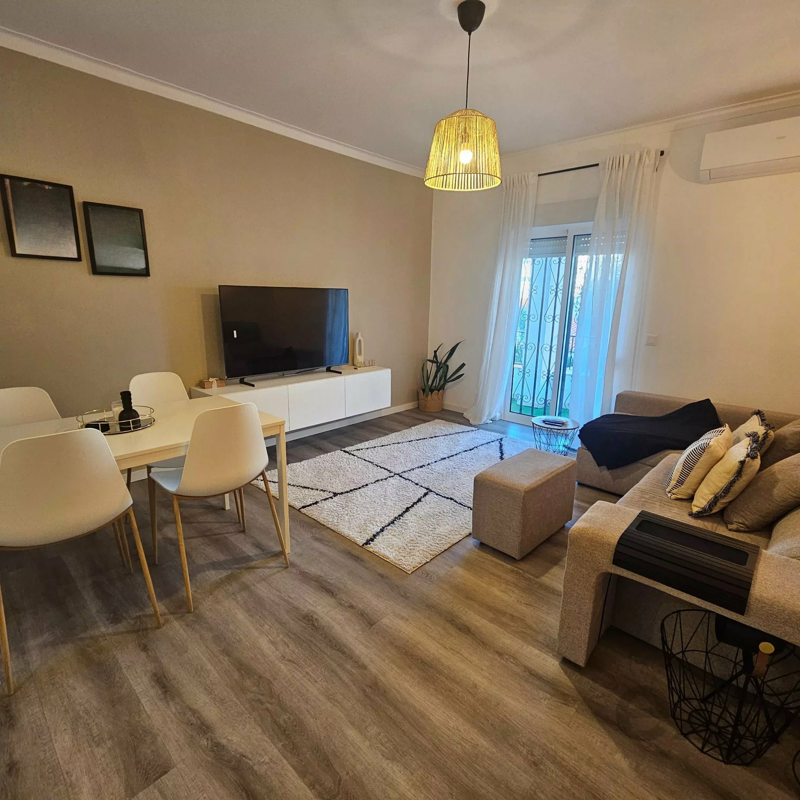 Contemporary living room with a woven pendant light, TV on a white media unit, and a cream sofa area. a statement rug and pale walls nearby.
