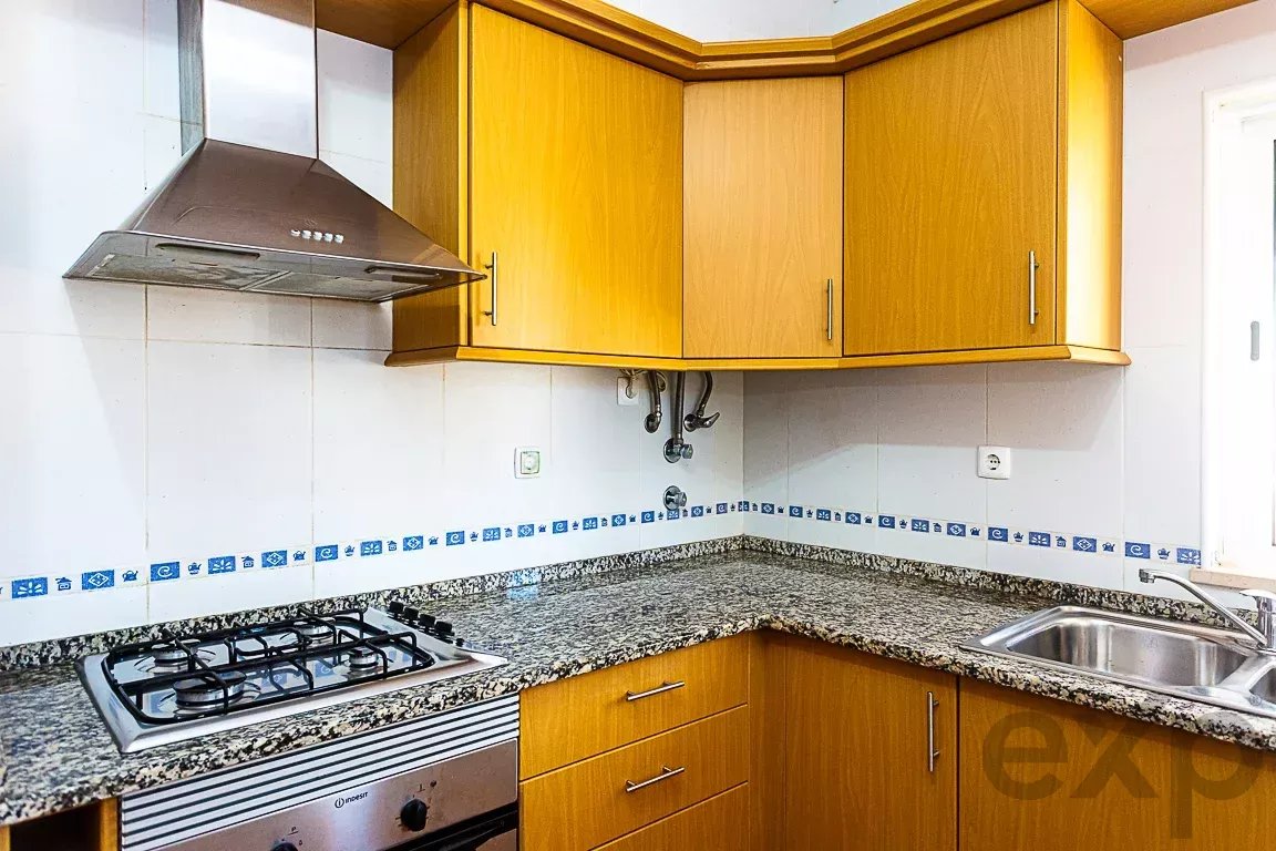 L-shaped kitchen with wooden cabinets, granite countertop, gas stovetop, and a stainless range hood above it.