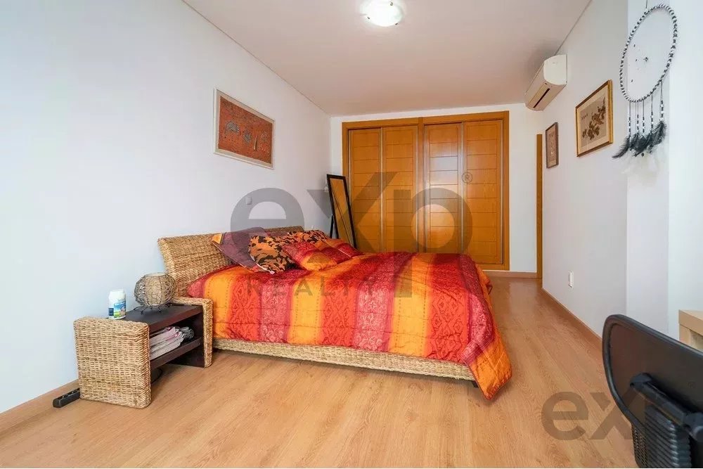 Wicker-framed bed with orange-red quilt in a bright bedroom, with a wooden closet behind and a small nightstand beside it.