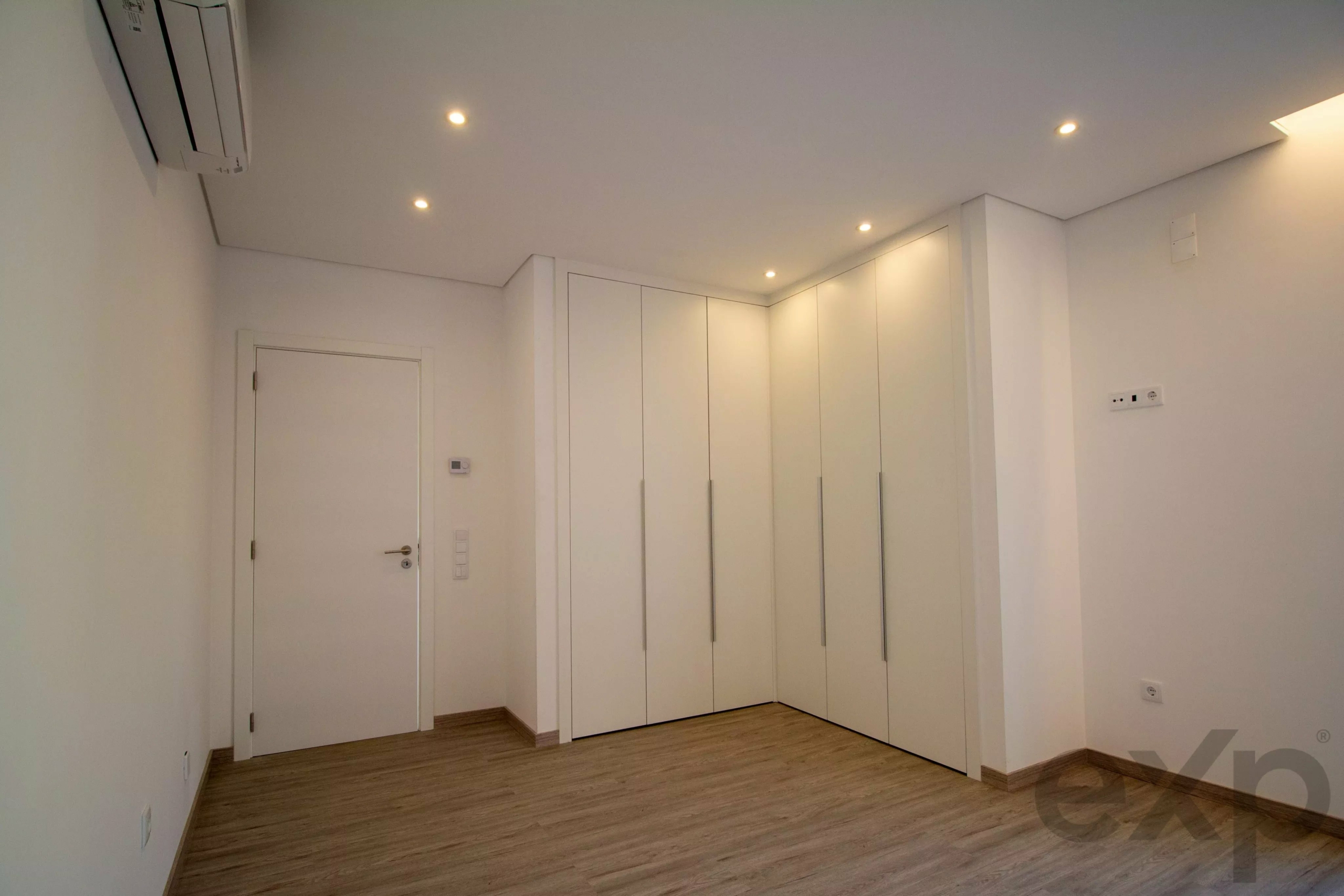 Modern white hallway with tall built-in wardrobes along the right wall and a wooden floor.