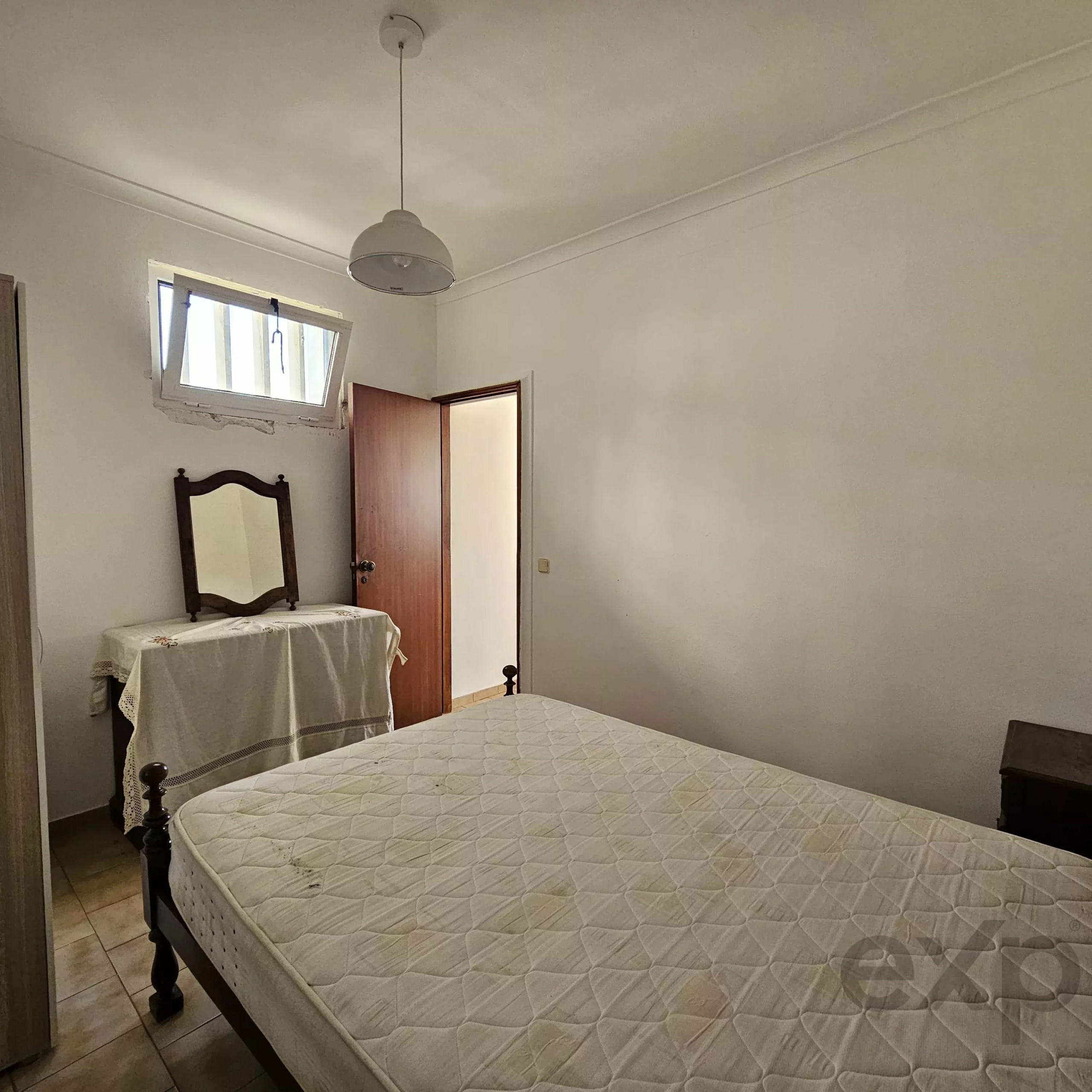 Small hotel-style bedroom with two single beds, white quilts, and a wooden mirror against the left wall near a window.