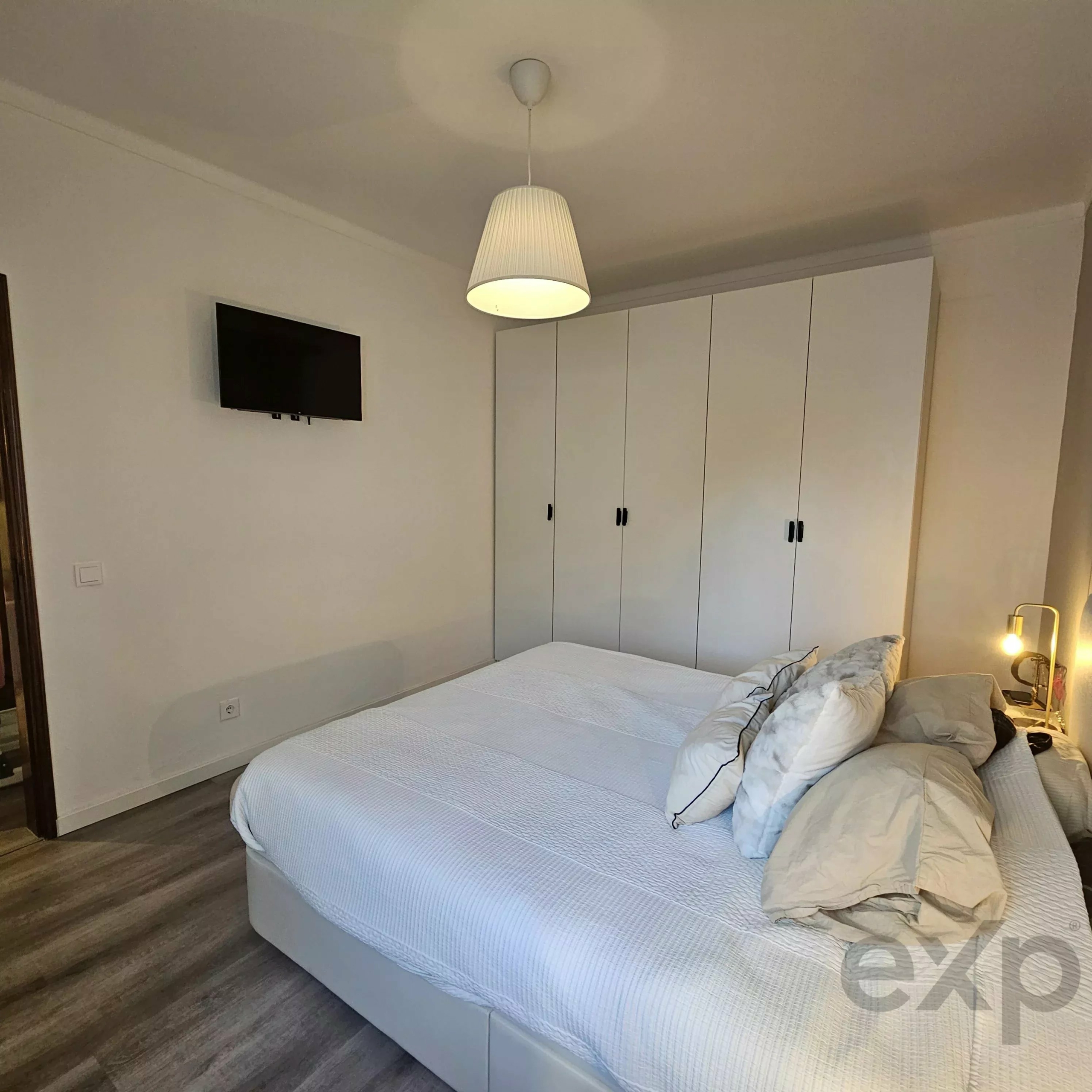Twin bedroom with two white beds, tall white wardrobes, and a hanging pendant light.