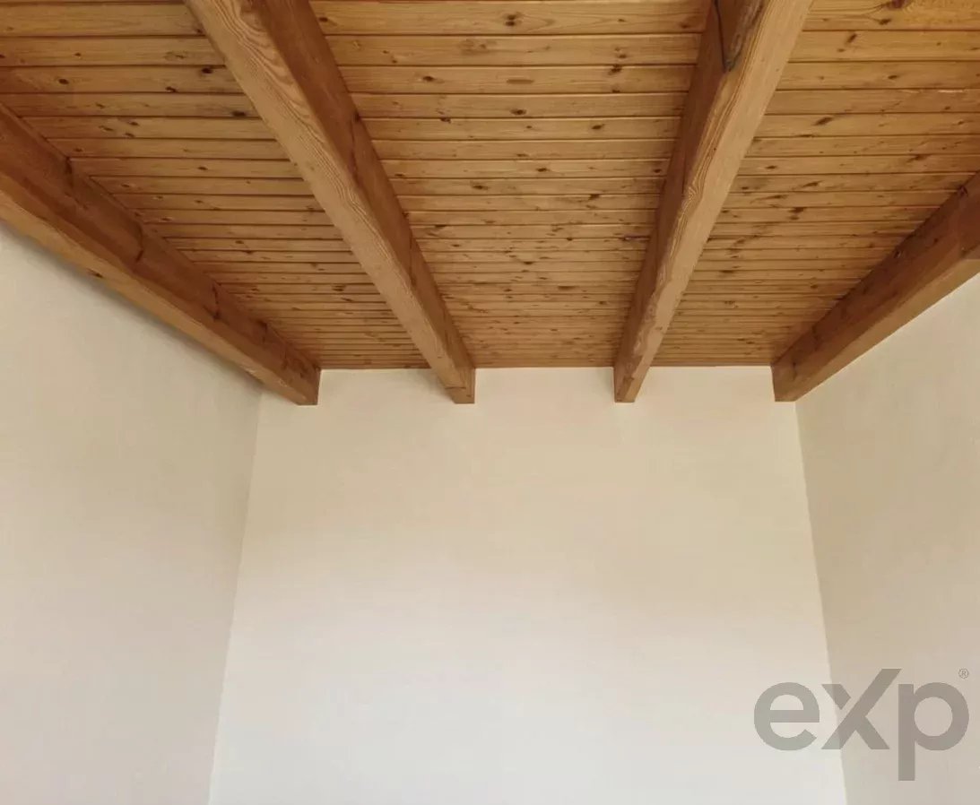 Exposed wooden ceiling beams meeting at a white cornered wall, viewed from below in a room.