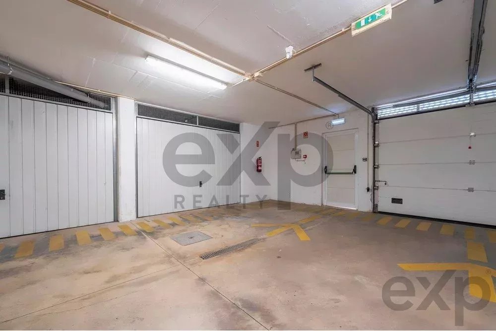 Interior of an industrial garage with white roll-up doors, concrete floor, and yellow parking markings under fluorescent lights on the ceiling