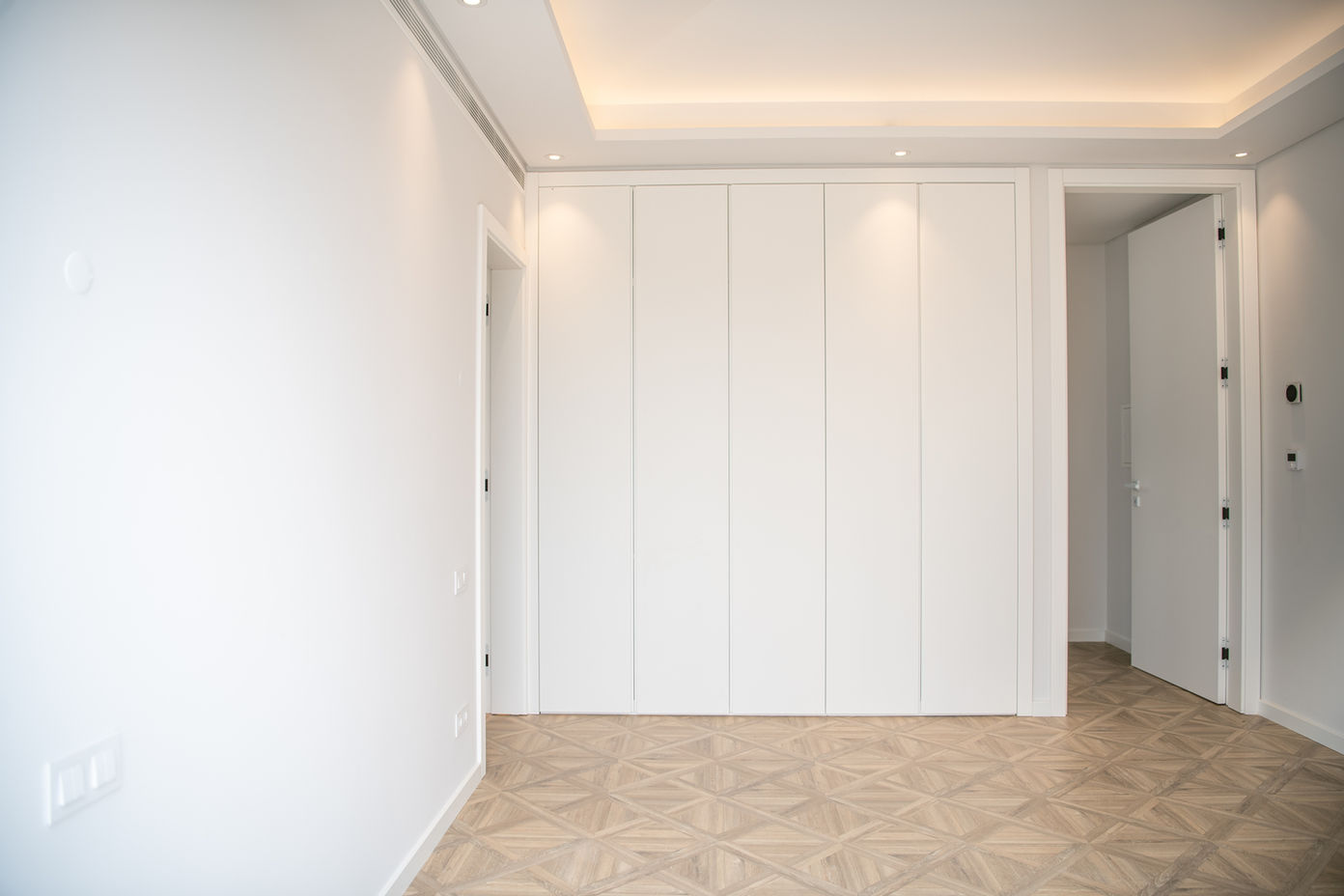 29bf52_002bc9d3ea8b47d1be70f780e91ff477-mv2 Bright minimalist room with a large white built-in wardrobe and geometric wooden floor.