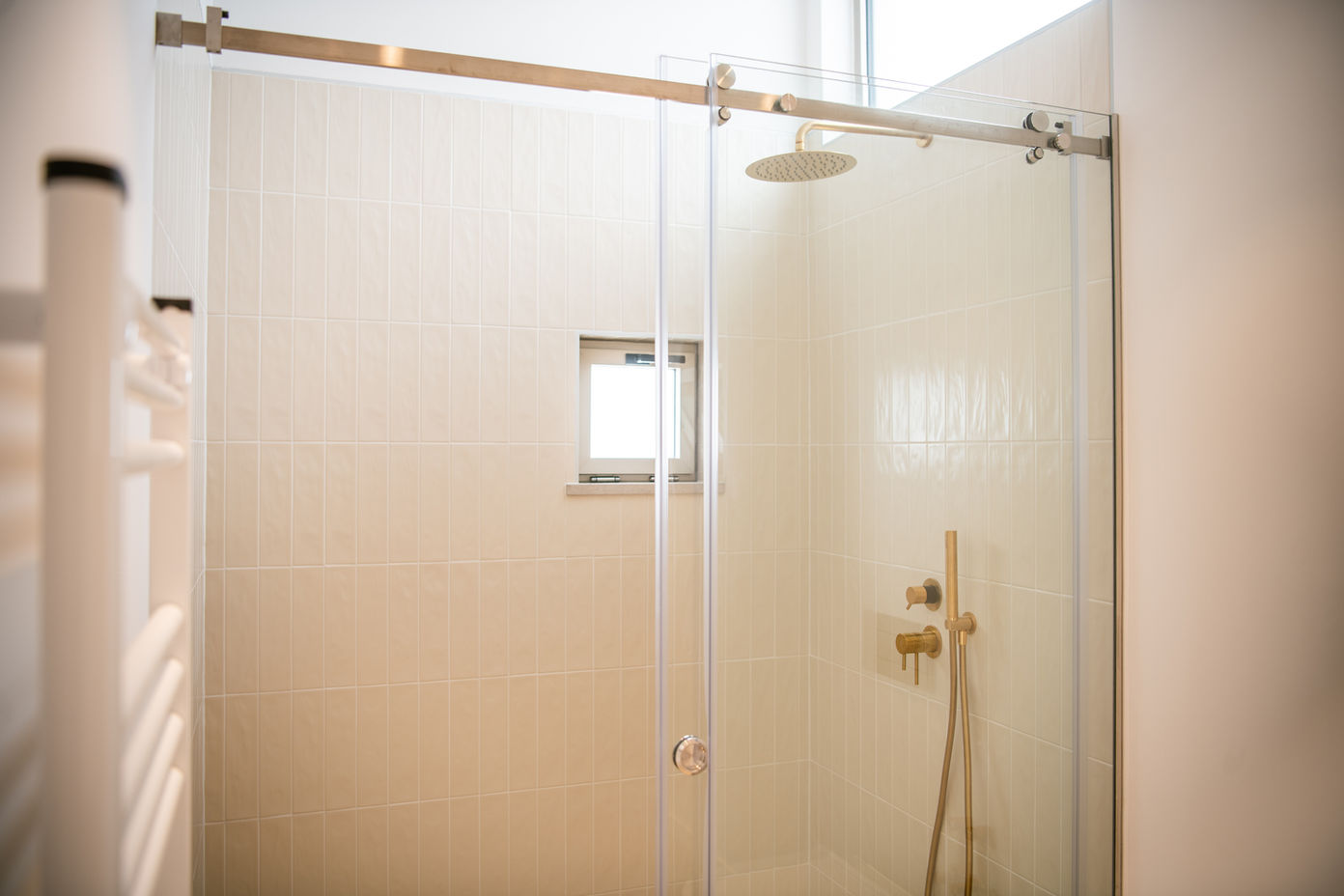 29bf52_b306ad6d276749d394159f4577850ce1-mv2 Glass-enclosed shower with brass fixtures and a rainfall showerhead in a tiled bathroom.