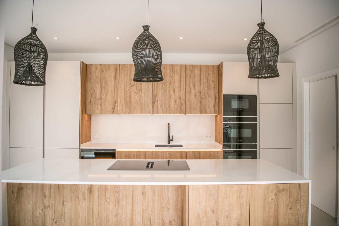 29bf52_c4379e2ef00745fe88f3aa8fff9875b8-mv2 Modern kitchen with white countertops, oak cabinets, and a central island with a built‑in cooktop.