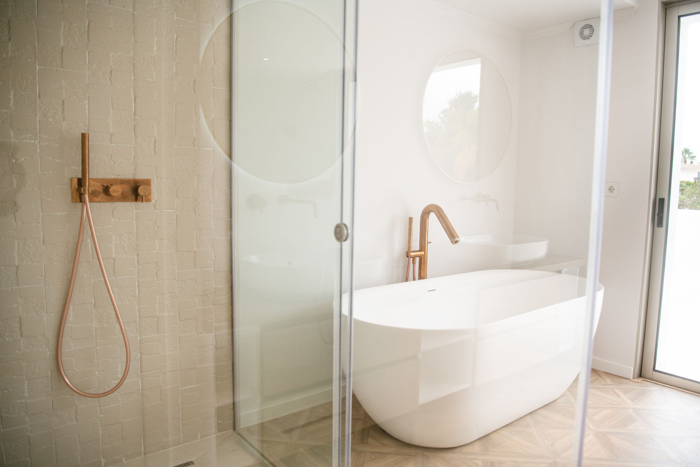 29bf52_f4ae0d511a8d4255afdcb6635b882906-mv2 Freestanding white bathtub with a rose-gold faucet beside a glass-enclosed shower in a bright bathroom.