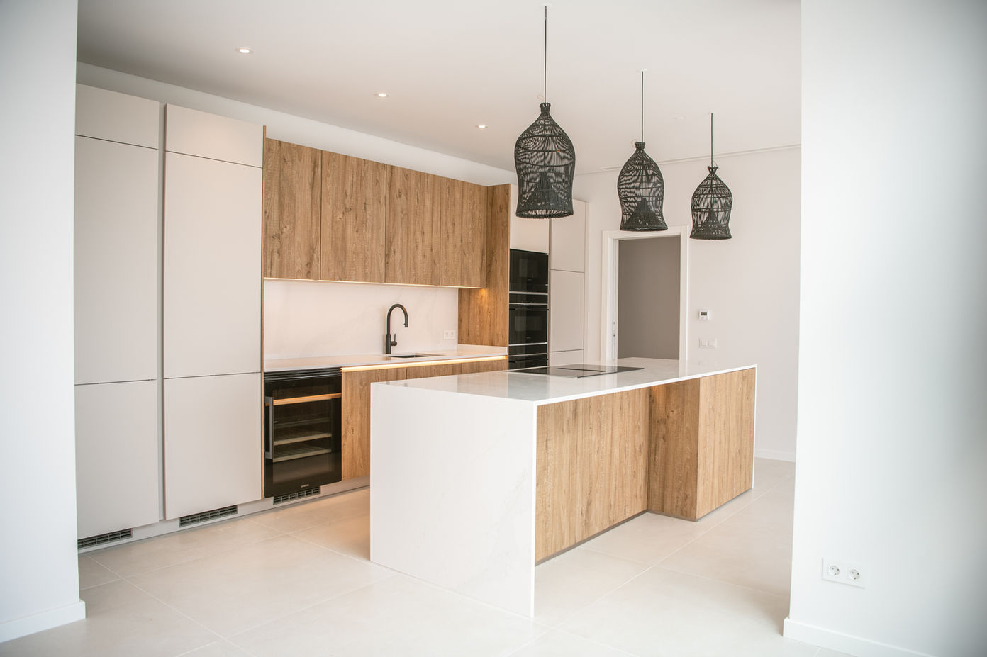 29bf52_f6e2d1b8c9e540eb804041846218aa91-mv2 Modern kitchen with white and wood cabinets, a large island, and three black pendant lights at the ceiling.