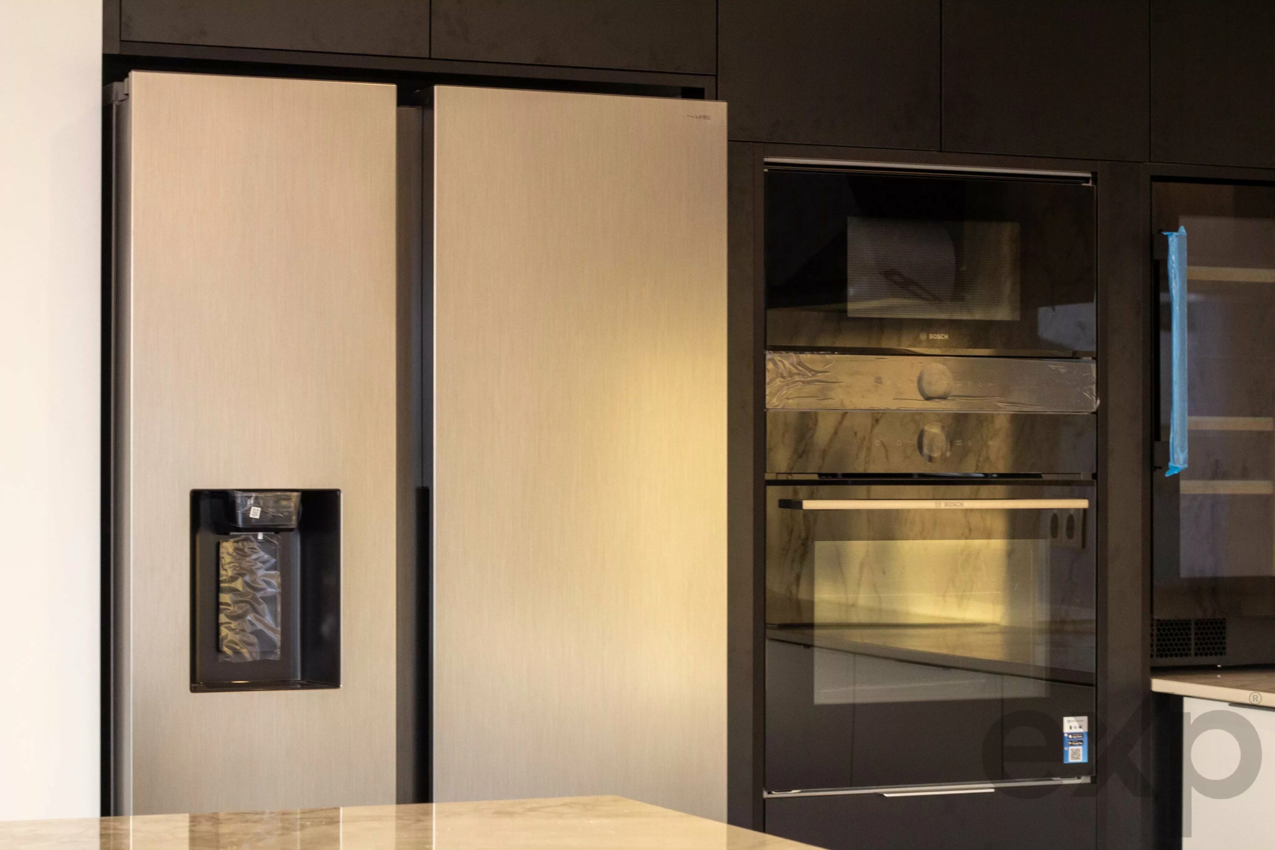 Modern kitchen with a tall stainless steel built-in refrigerator adjacent to dark cabinetry and a Bosch wall oven unit above a microwave/oven stack.