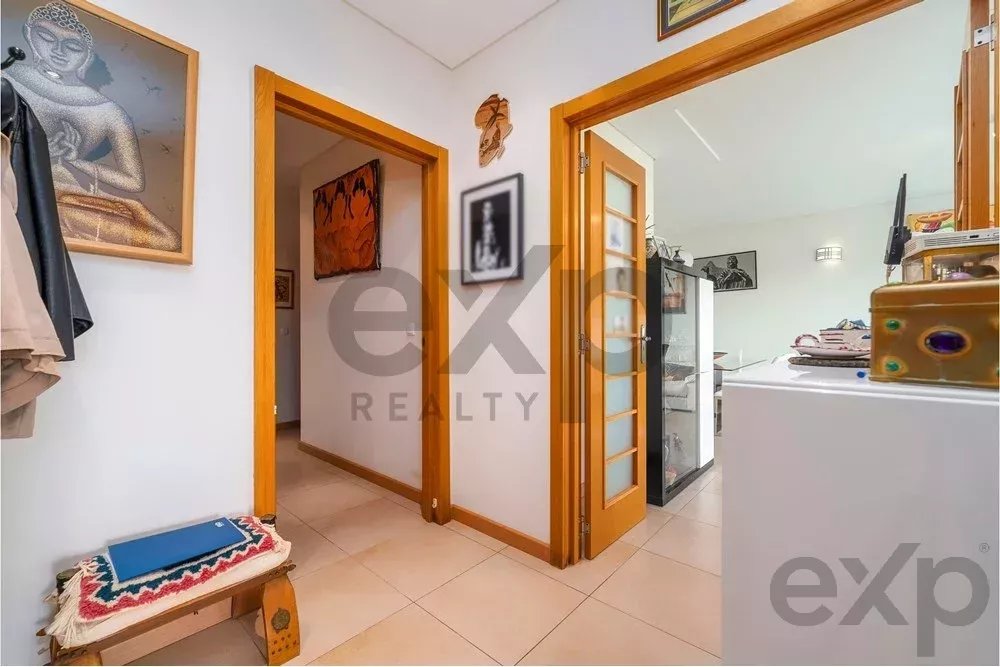 Bright hallway with wooden door frames, coats on the wall, and a bench with a blue book near the tiled floor.