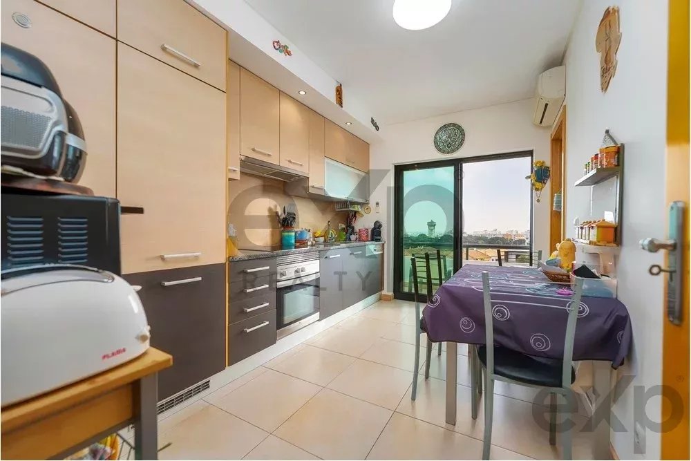 Modern kitchen with light wood cabinets, stainless appliances, and a purple-tableclothed dining table near a balcony door stationing four chairs.