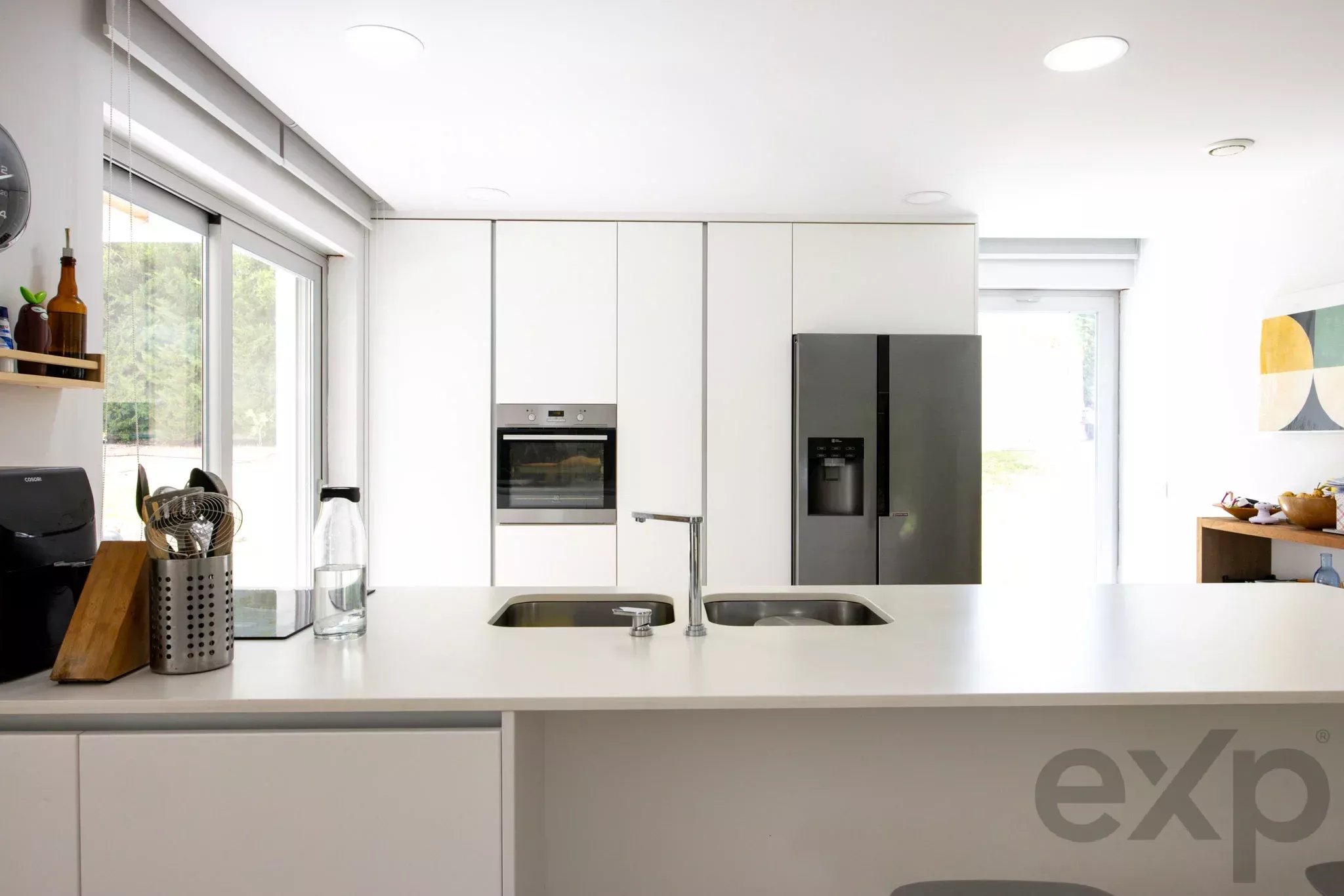 Bright white kitchen with an island, double sink, and stainless steel fridge and oven.