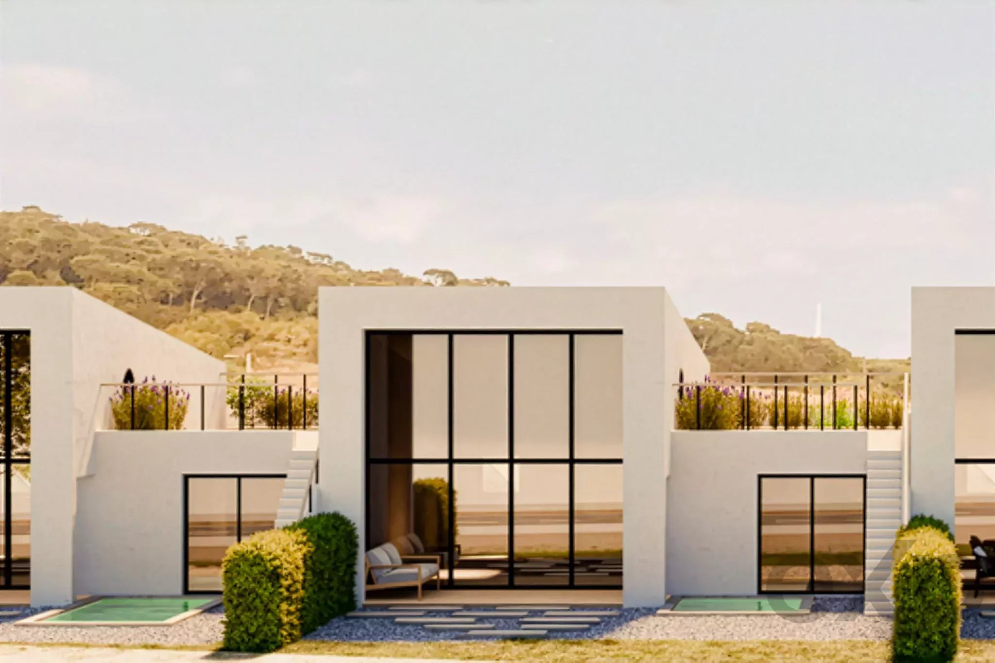 Modern white building with large glass windows and outdoor seating, hills in the background.