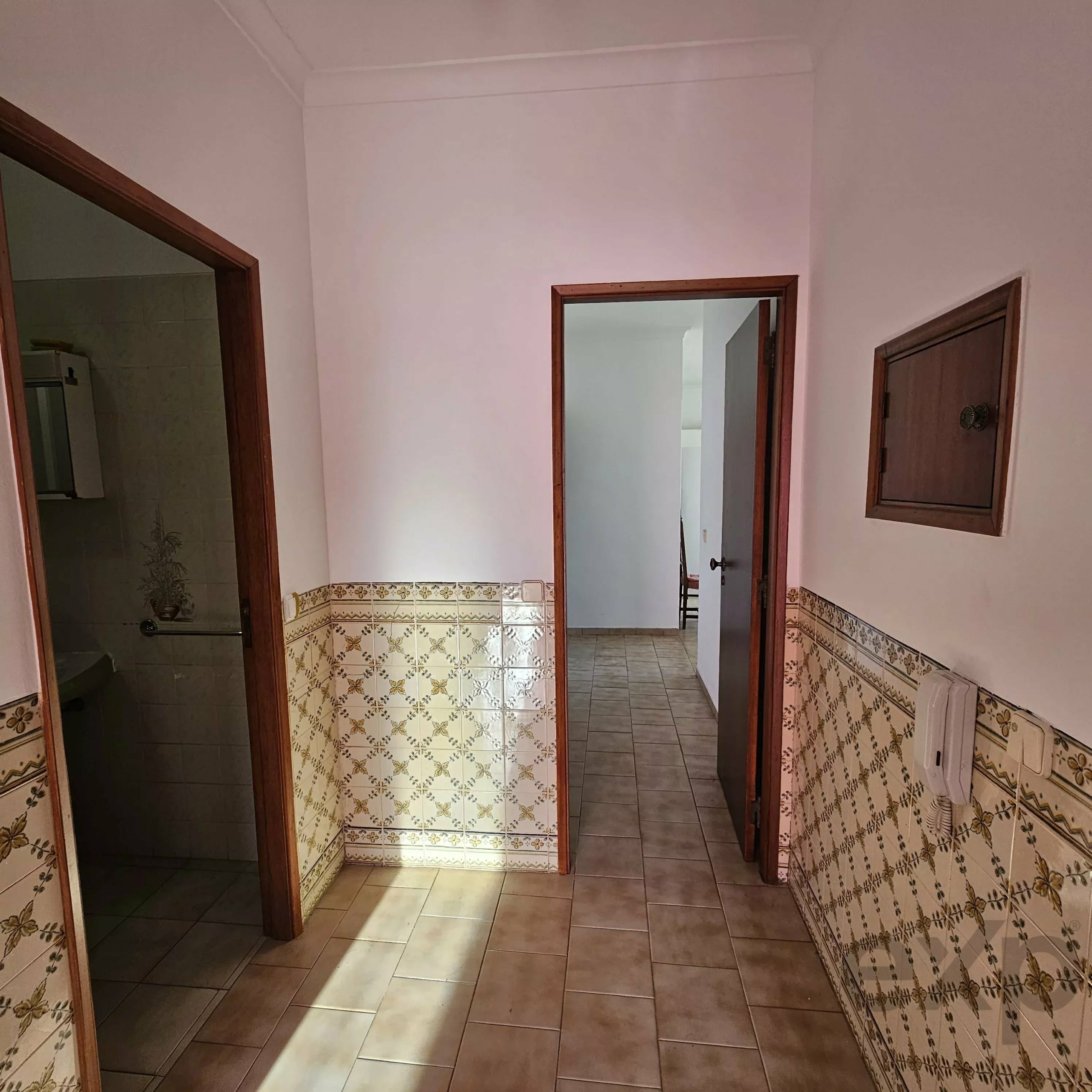 Interior hallway with beige walls, wooden door frames, and tiled wainscoting featuring a floral pattern at the bottom edge.