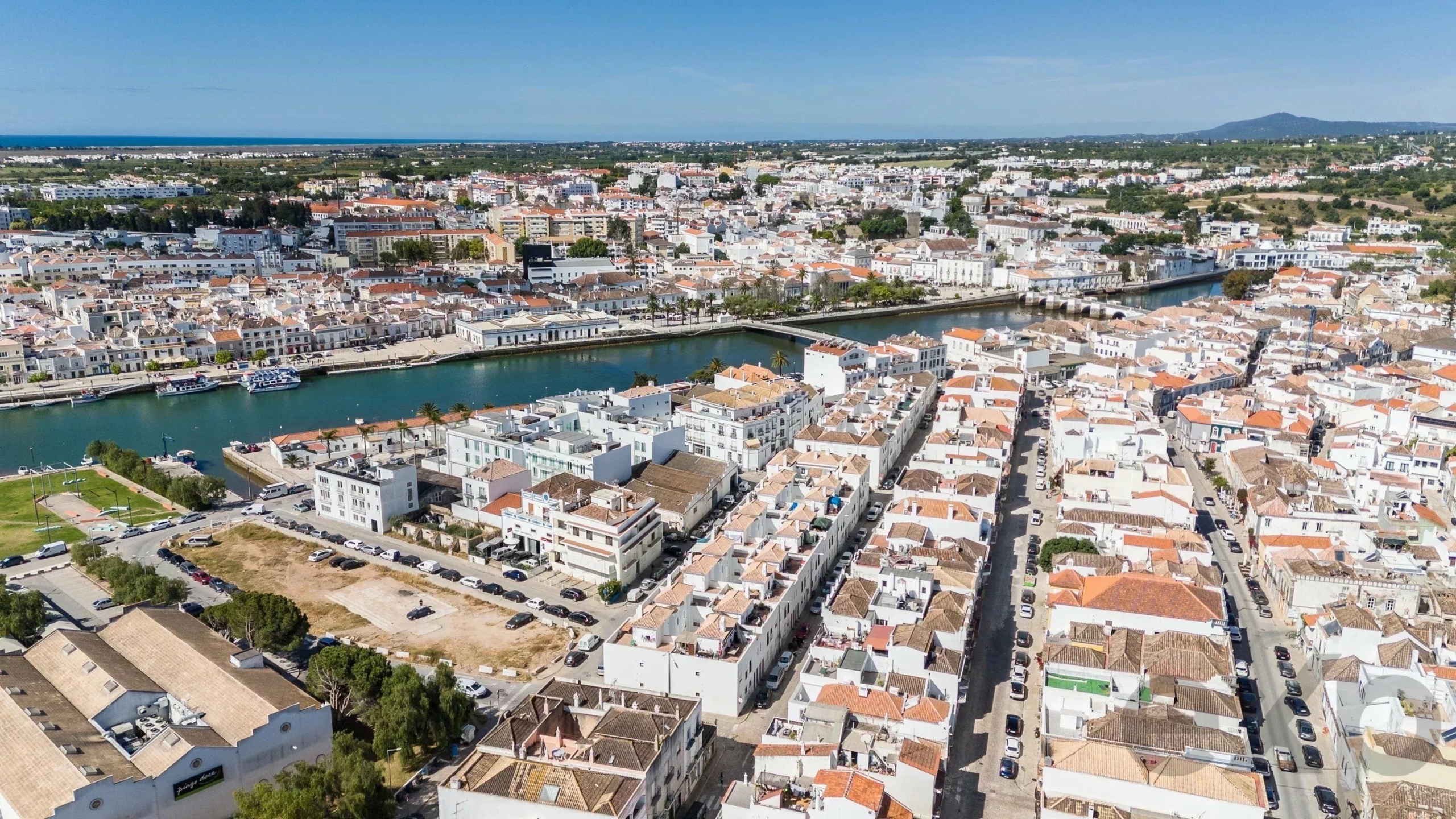 Aerial view of a coastal town with white buildings, red-tiled roofs, and a canal lined with boats near the sea.