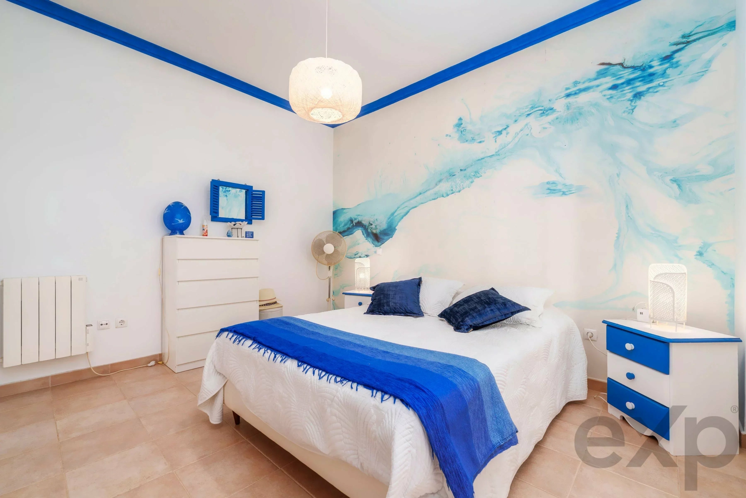 Bright bedroom with white walls and blue decor, bed with white quilt and blue throws, blue dresser and blue wall mural.
