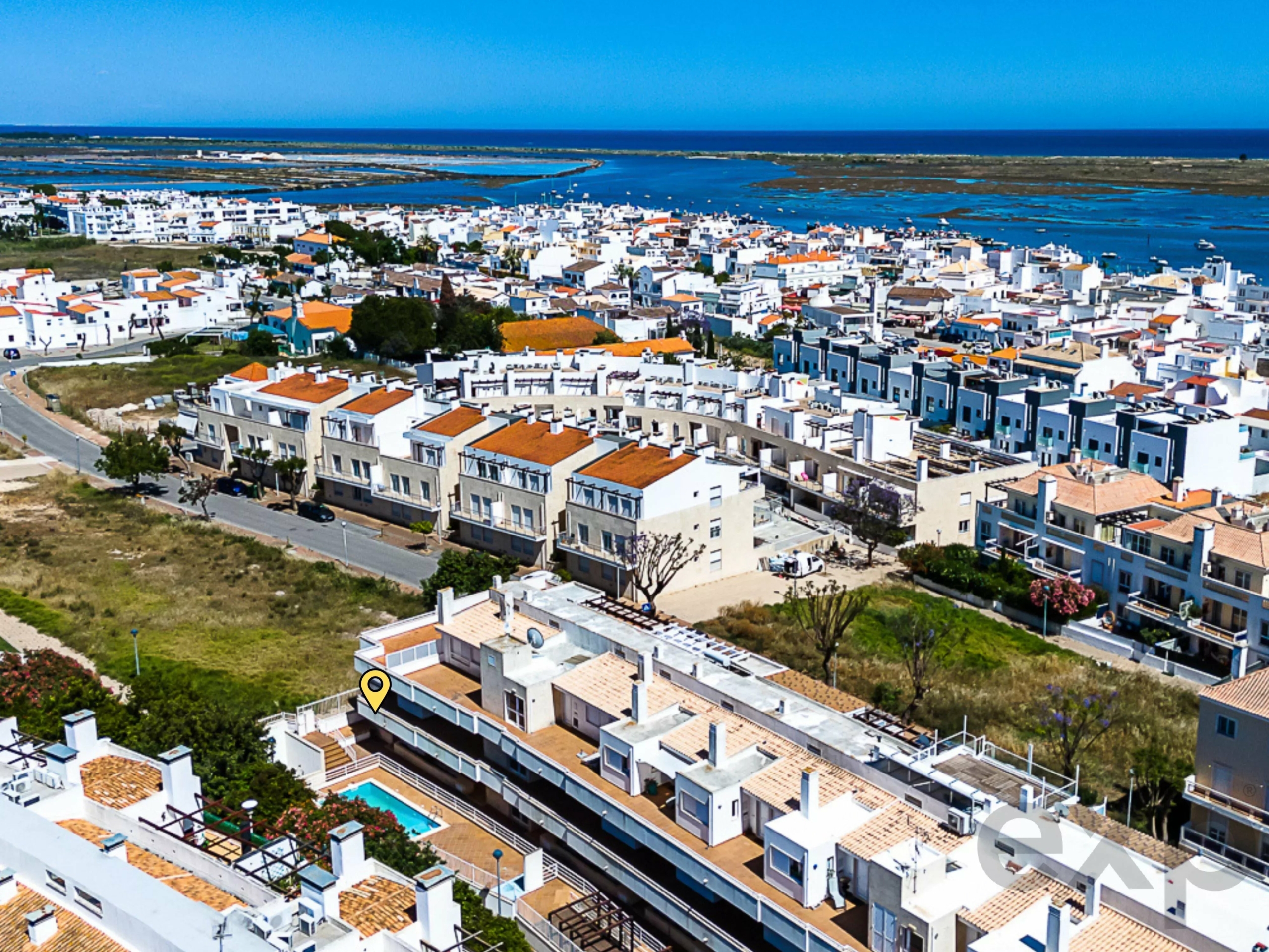 Aerial view of a white-walled coastal town with orange roofs along the shoreline and blue sea.
