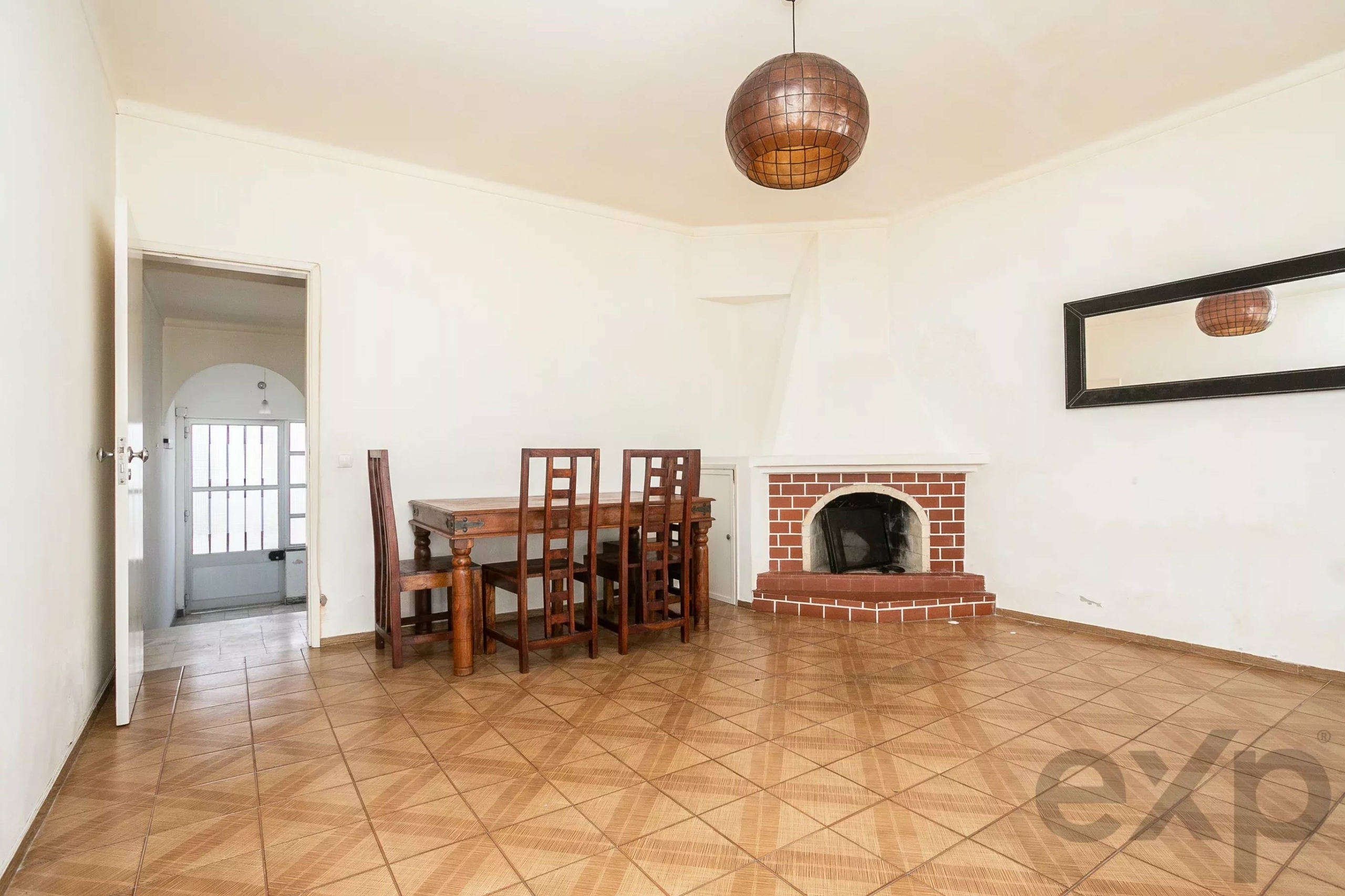 Dining room with a wooden table and tall chairs beside a brick fireplace and a round copper pendant light above.
