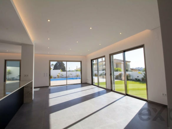 Bright open living area with large floor-to-ceiling windows overlooking a pool and yard outside, natural light flooding the space.