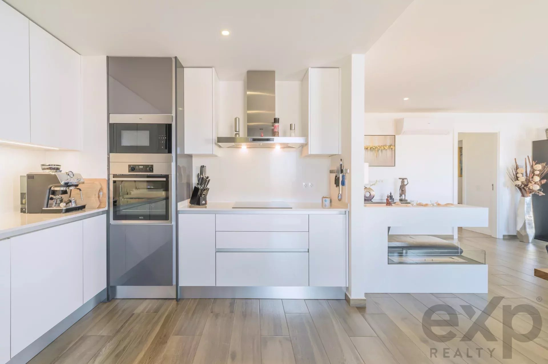 Modern white kitchen with built-in stainless steel oven, microwave, and range hood, light wood floor
