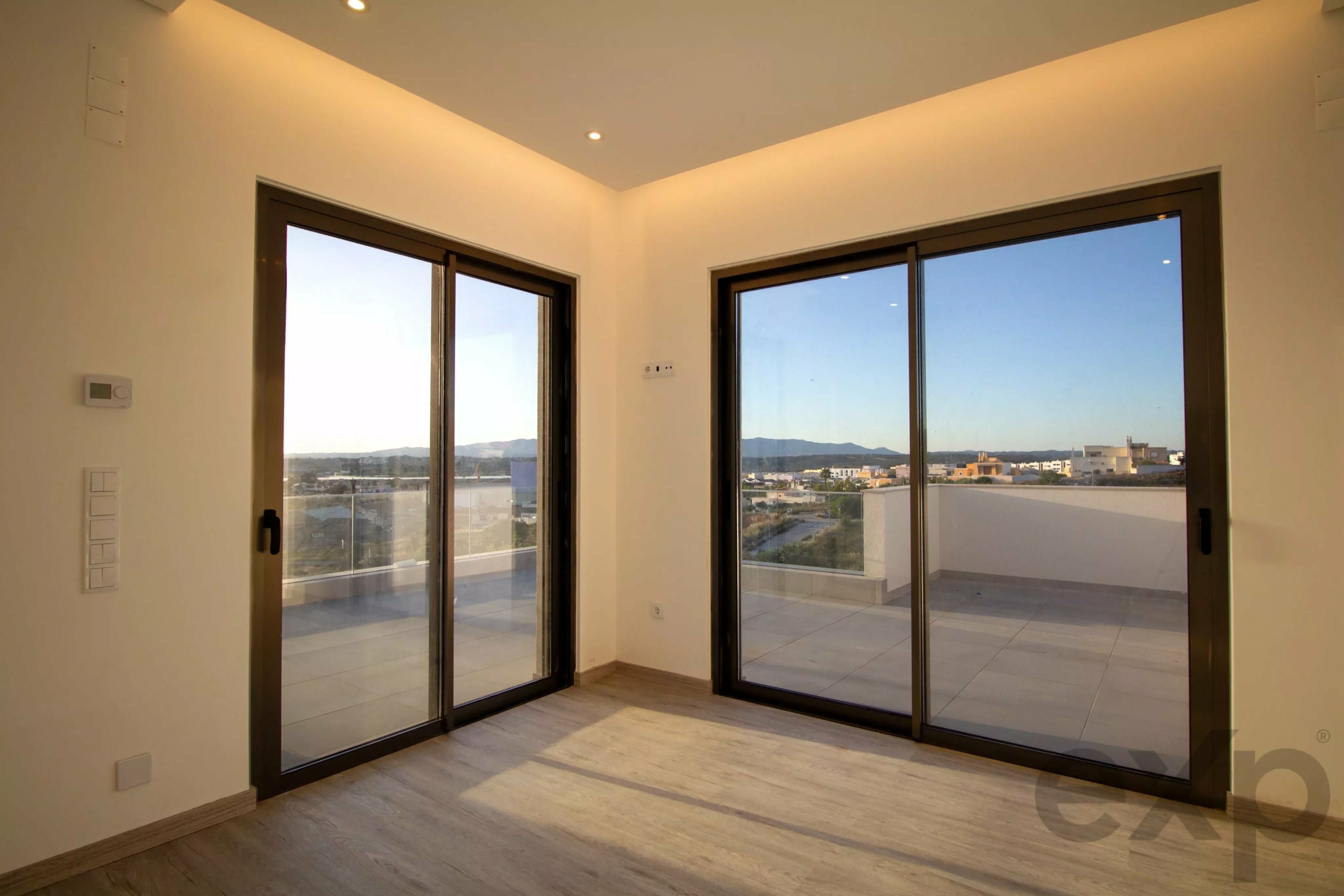 Corner of a bright modern room with large black-framed sliding glass doors opening to a balcony and cityscape beyond.