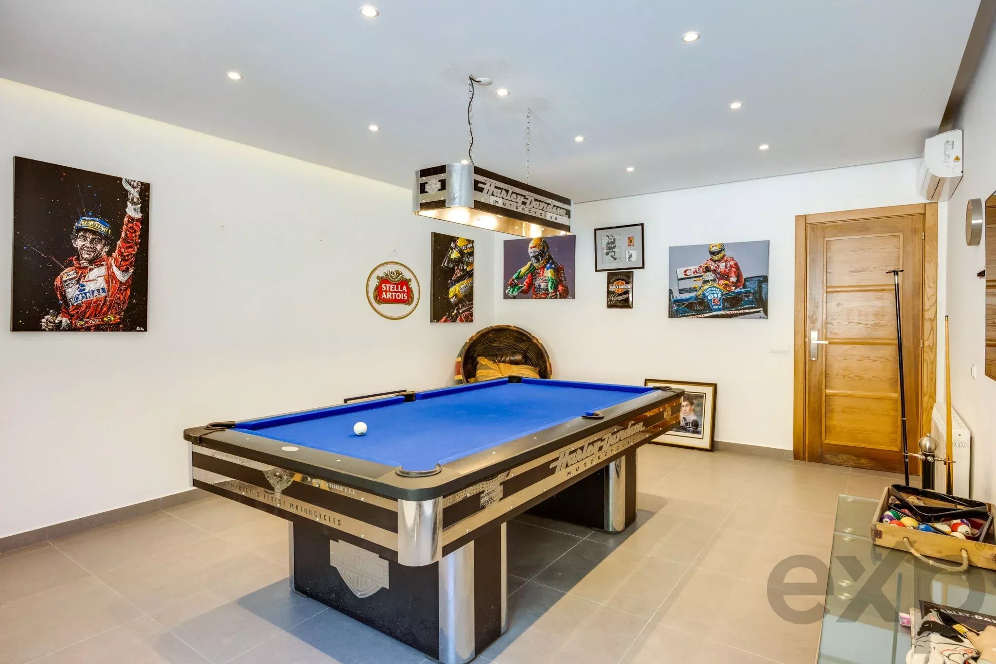 Blue-felt pool table in a room with racing-themed wall art and a wooden door in the background.