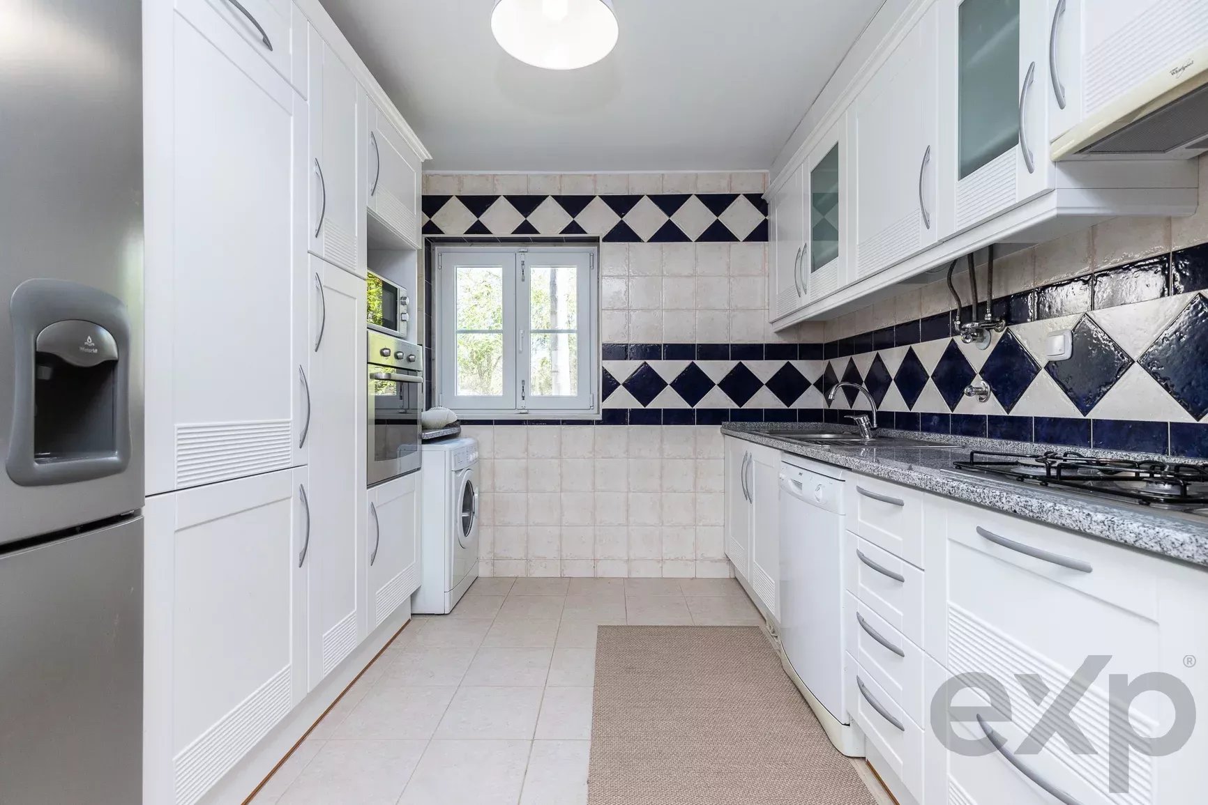 Bright white galley kitchen with a black-and-white diamond tile backsplash and modern cabinets along both sides.